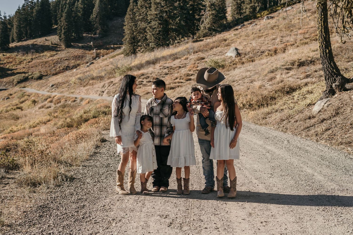 Family group gathered on a mountain trail surrounded by pine trees and rolling hills.