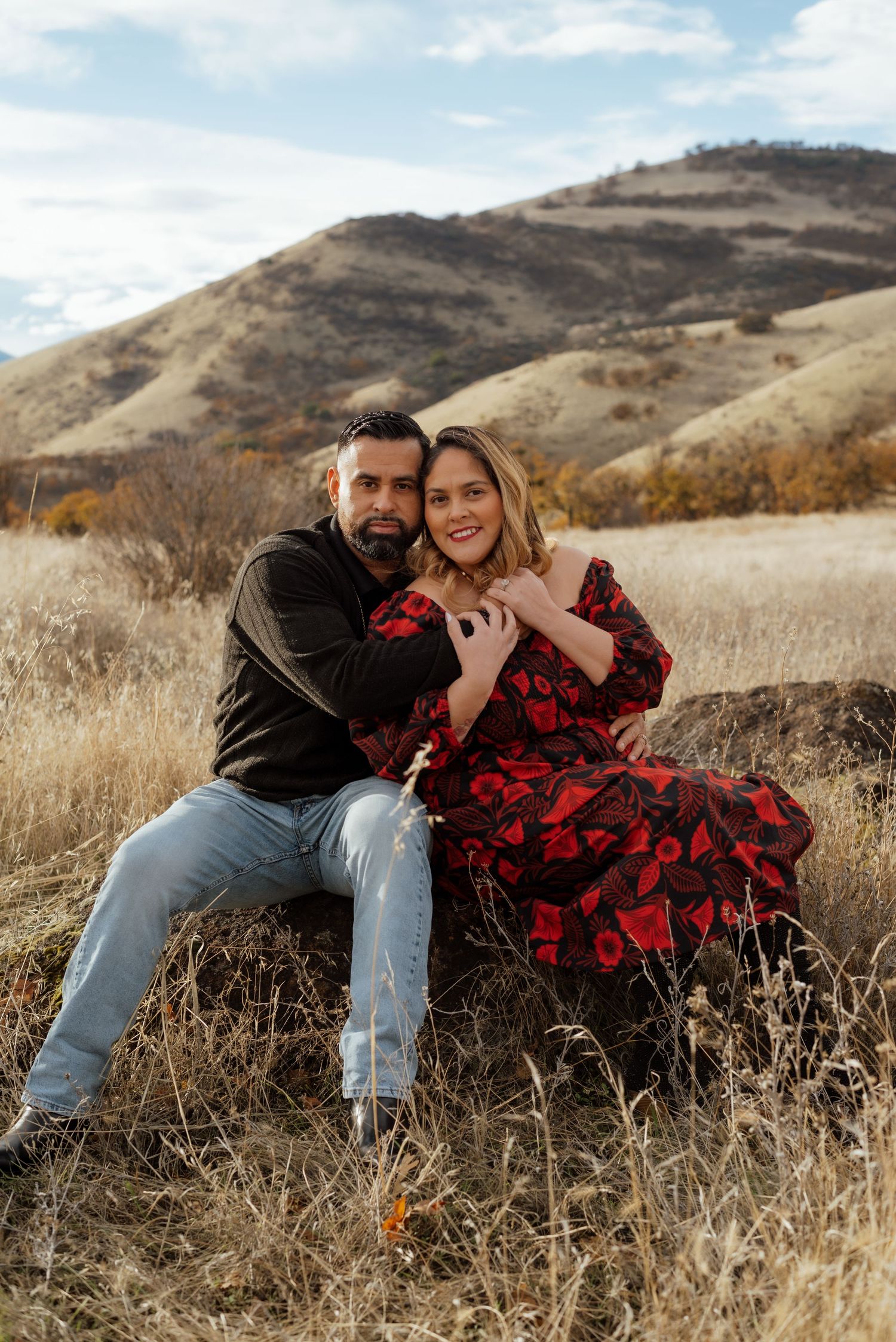 Couple embraces in golden autumn field with mountain backdrop.