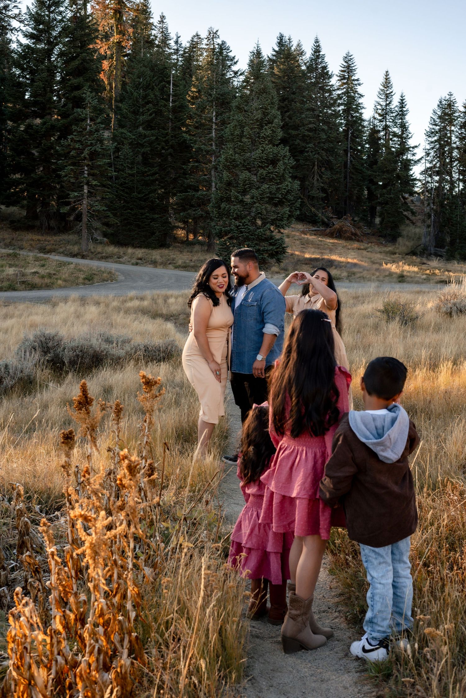 Family gathering on a mountain trail during sunset with tall grass and pine trees.