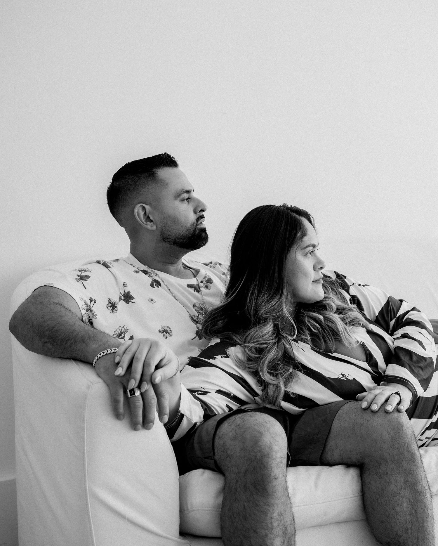 A black and white photo captures two people sitting close together on a white sofa.