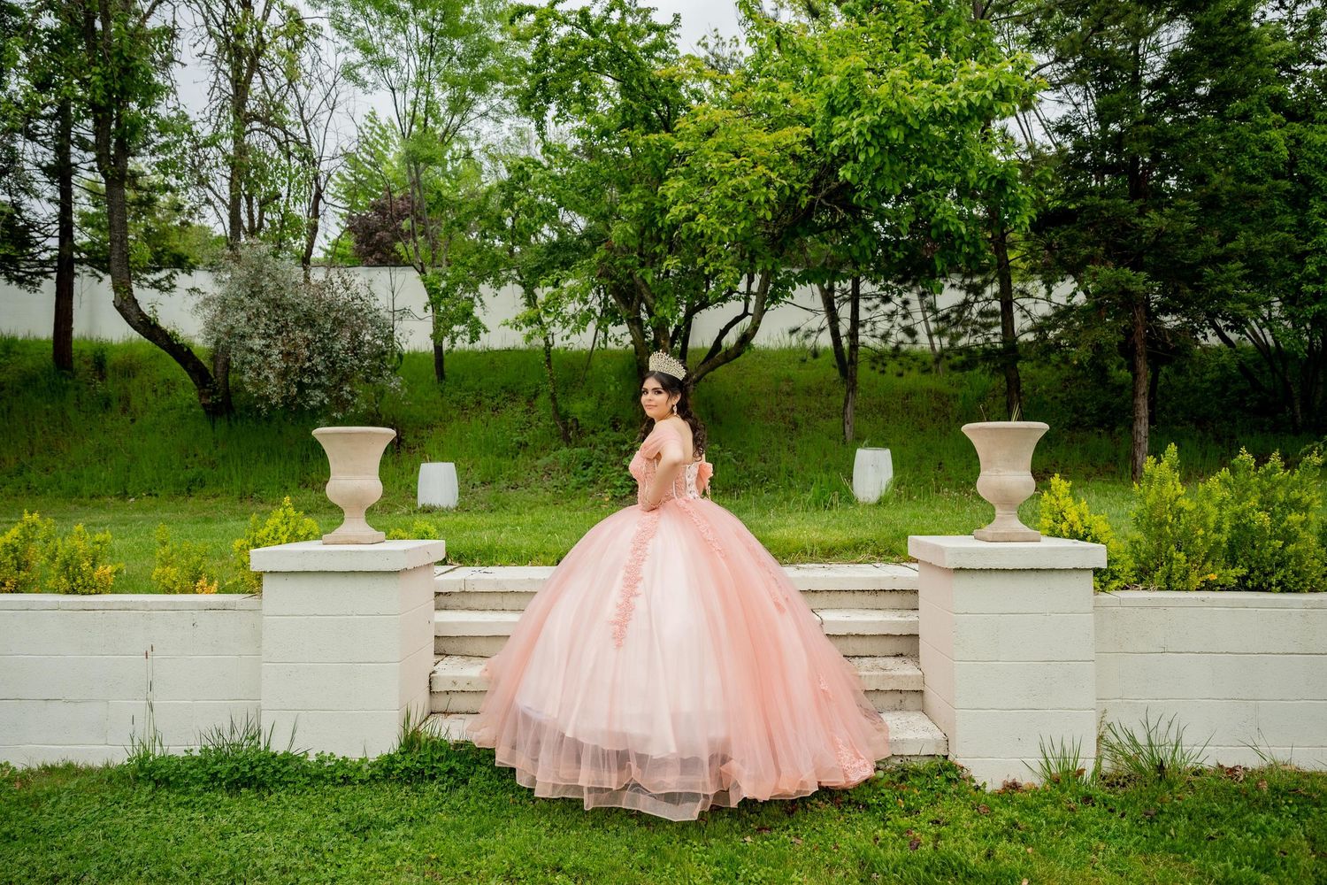 Dramatic peach ball gown photographed on stone steps surrounded by greenery.