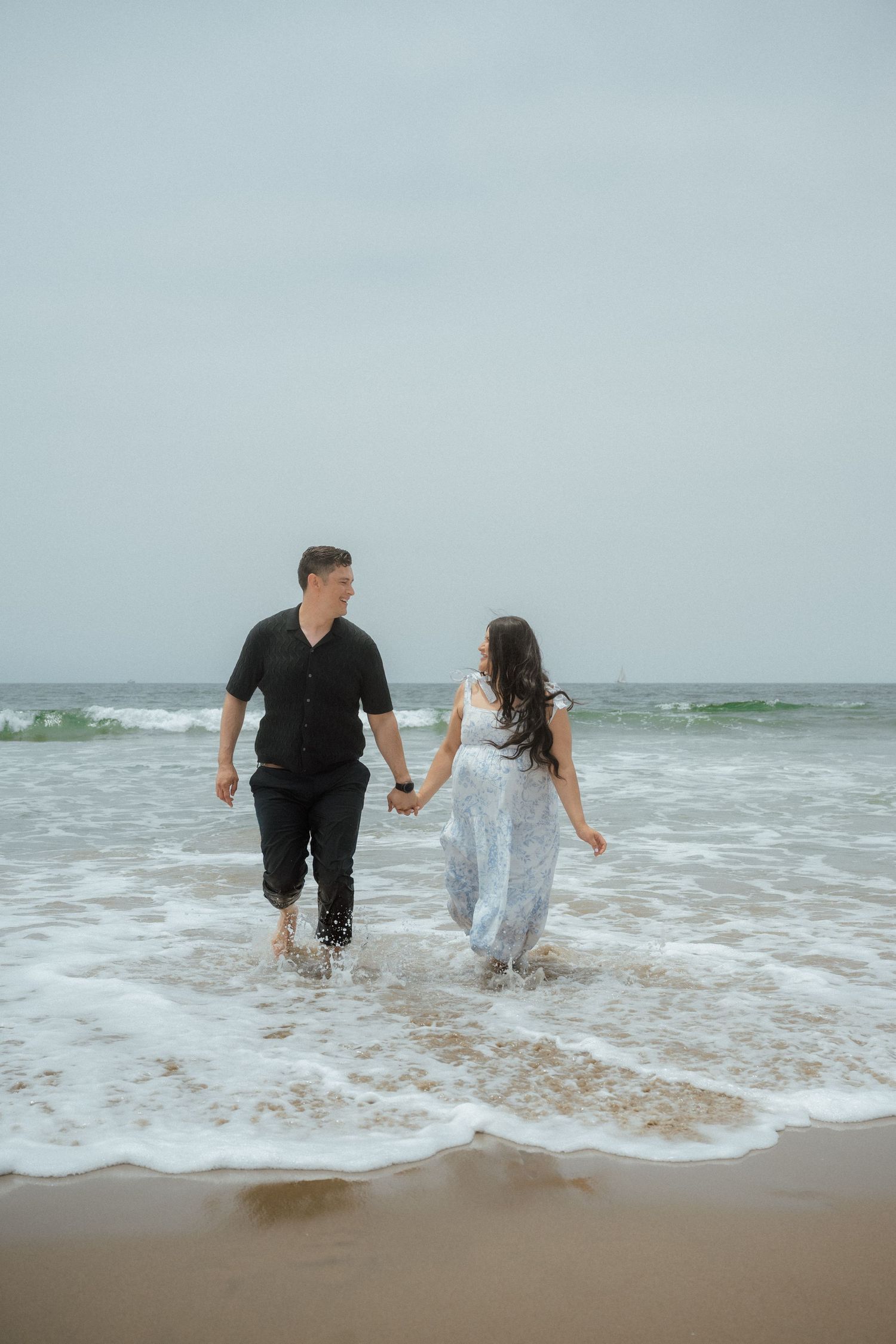 A couple plays in the ocean waves at the beach on an overcast day.