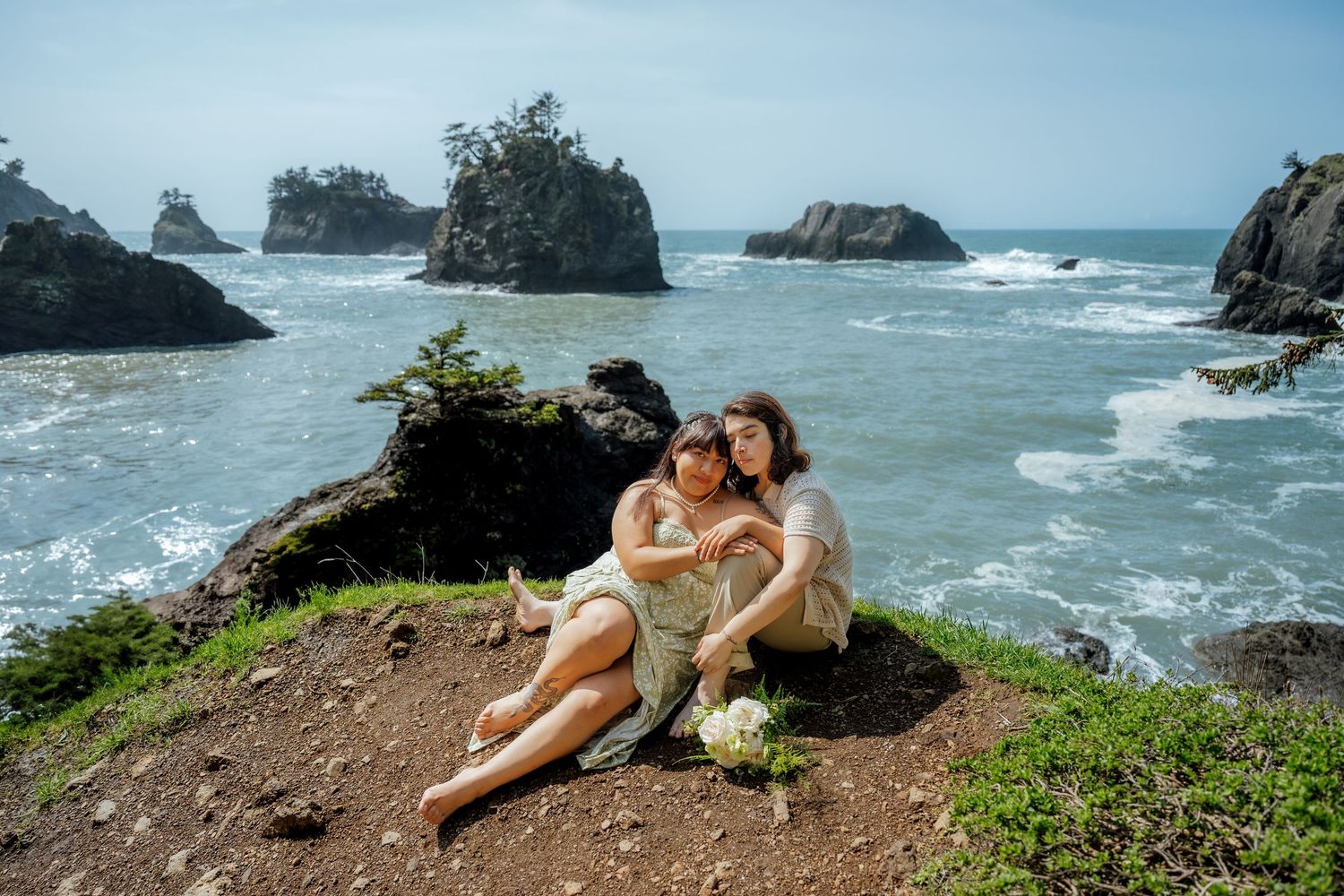 Couple relaxing on coastal cliff overlooking dramatic ocean scenery.