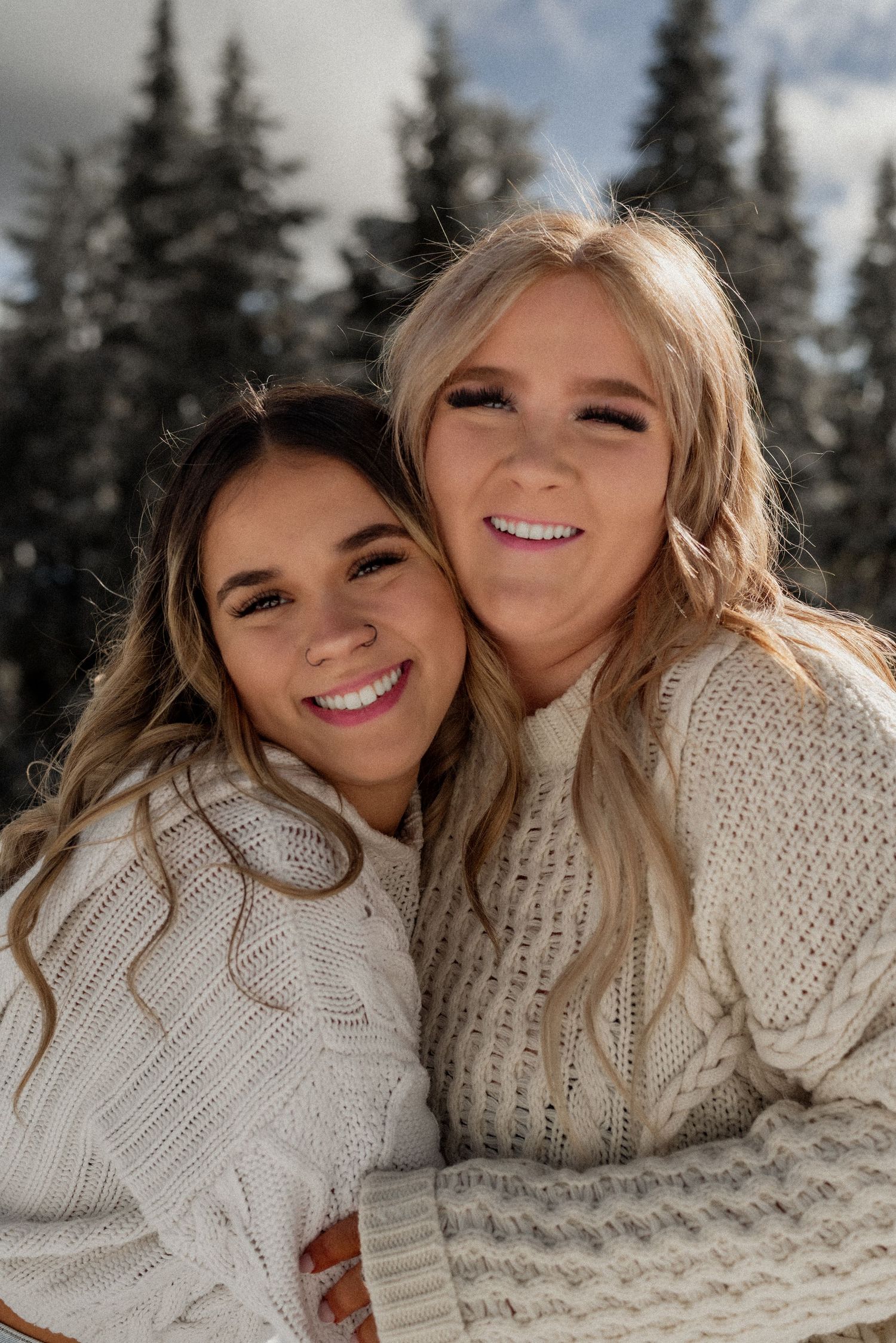 Two friends in matching cream cable knit sweaters share a joyful moment in a snowy winter setting.