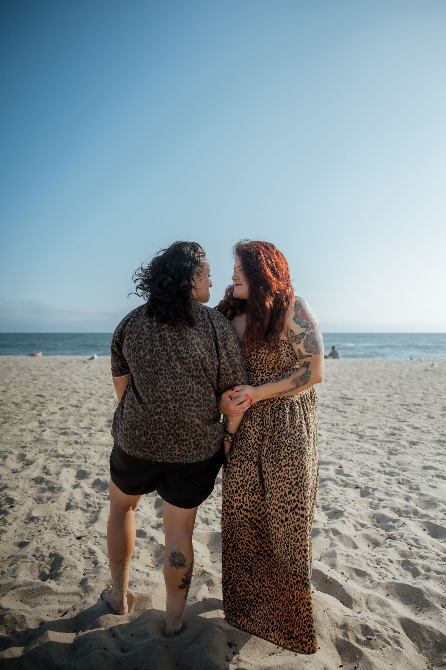 Two people in matching animal print outfits standing together on a sunny beach.