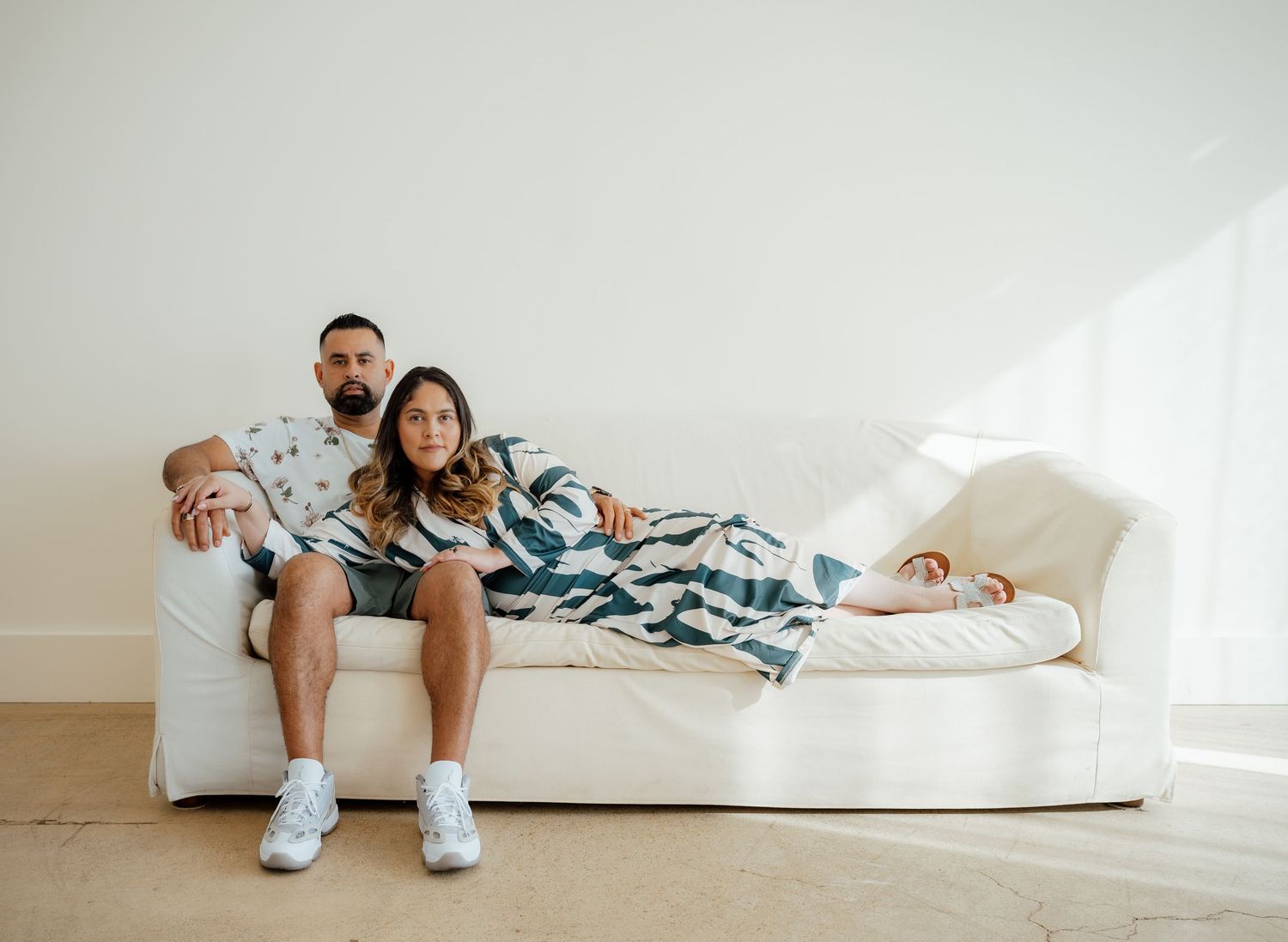 A couple shares a relaxed moment on a white couch in matching blue tie-dye outfits.