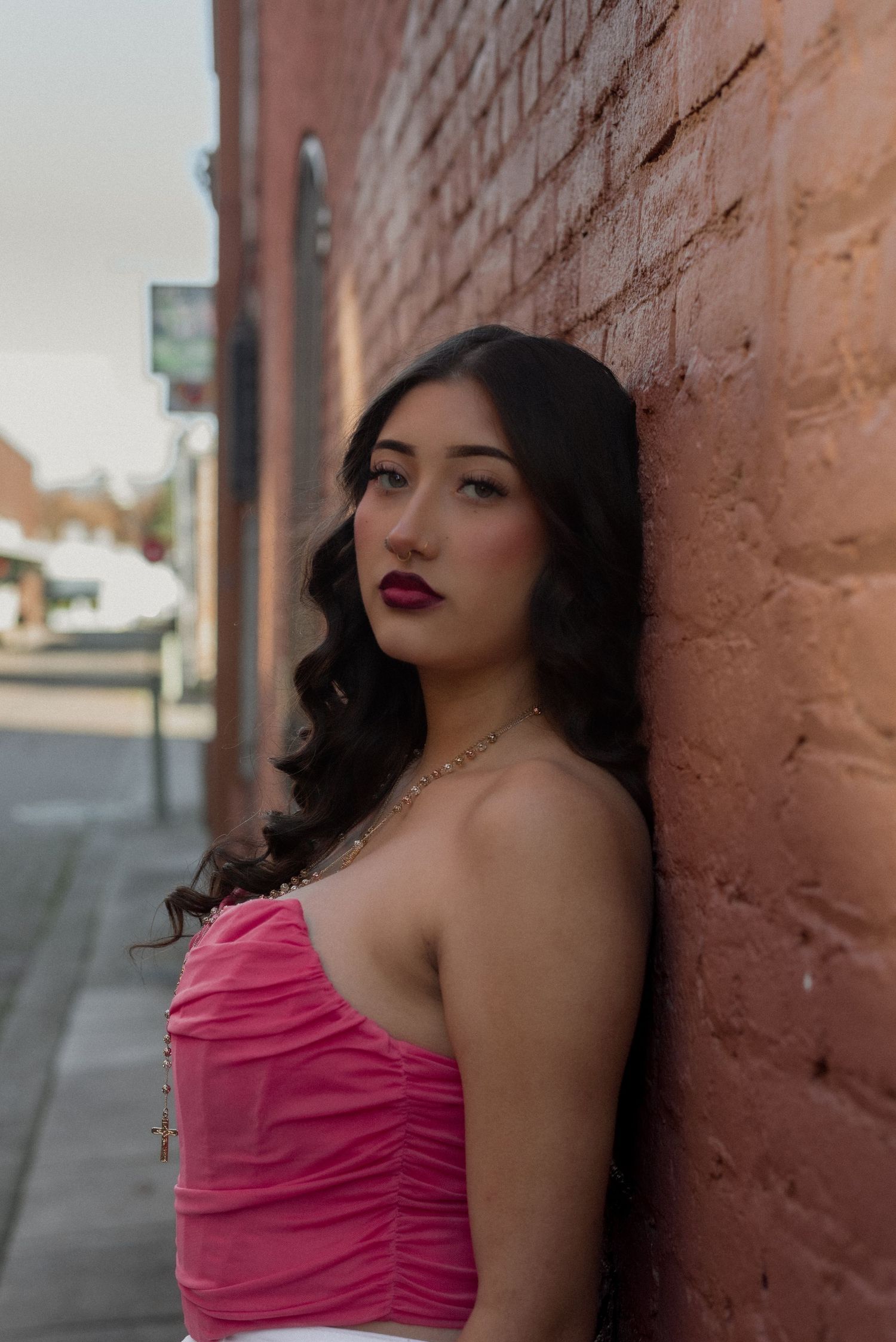 Portrait against a brick wall featuring a pink strapless top and glamorous makeup.