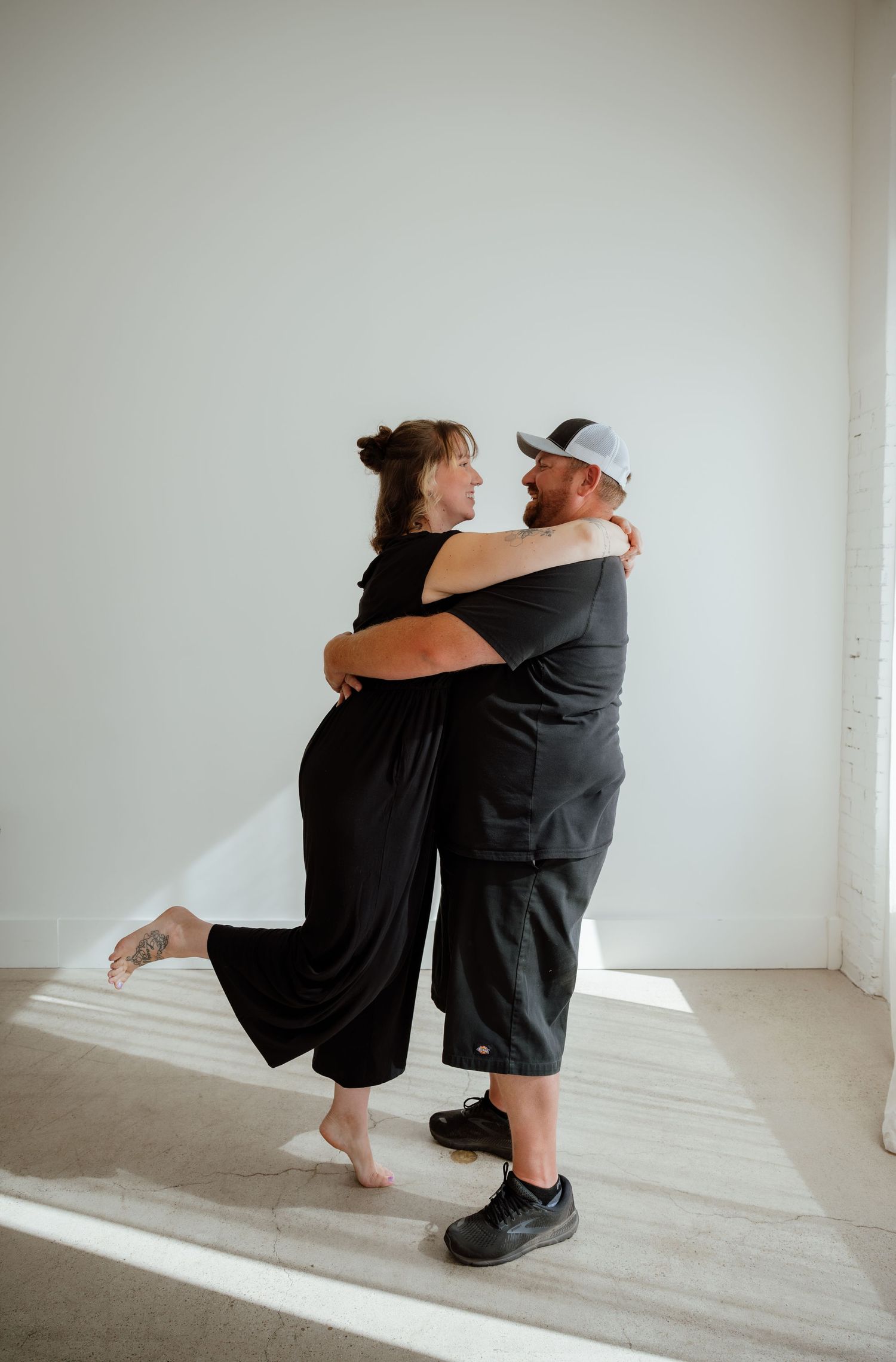 A couple dances together in a minimalist white room with natural lighting.