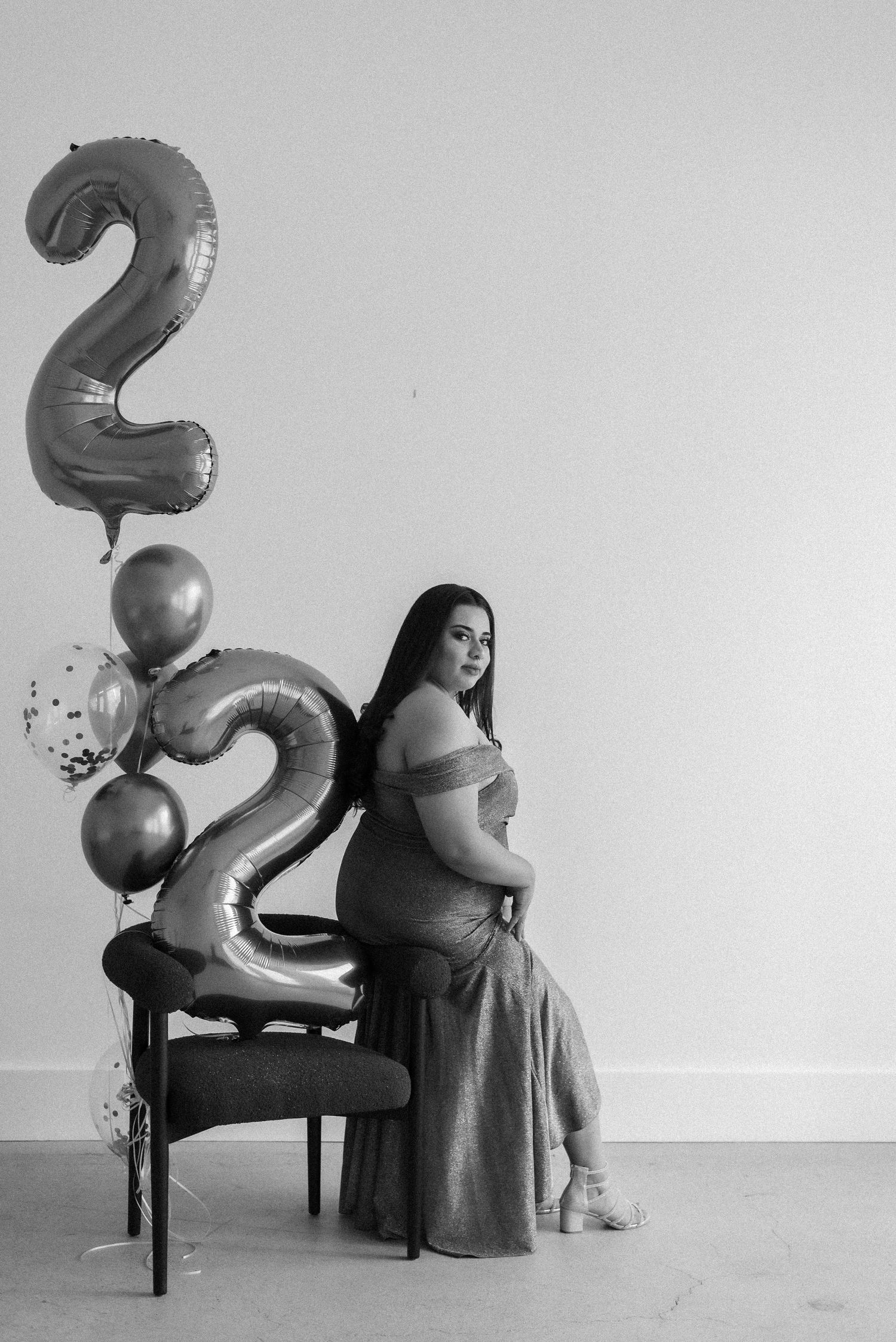 Black and white portrait with number 2 balloon and chair against plain background.
