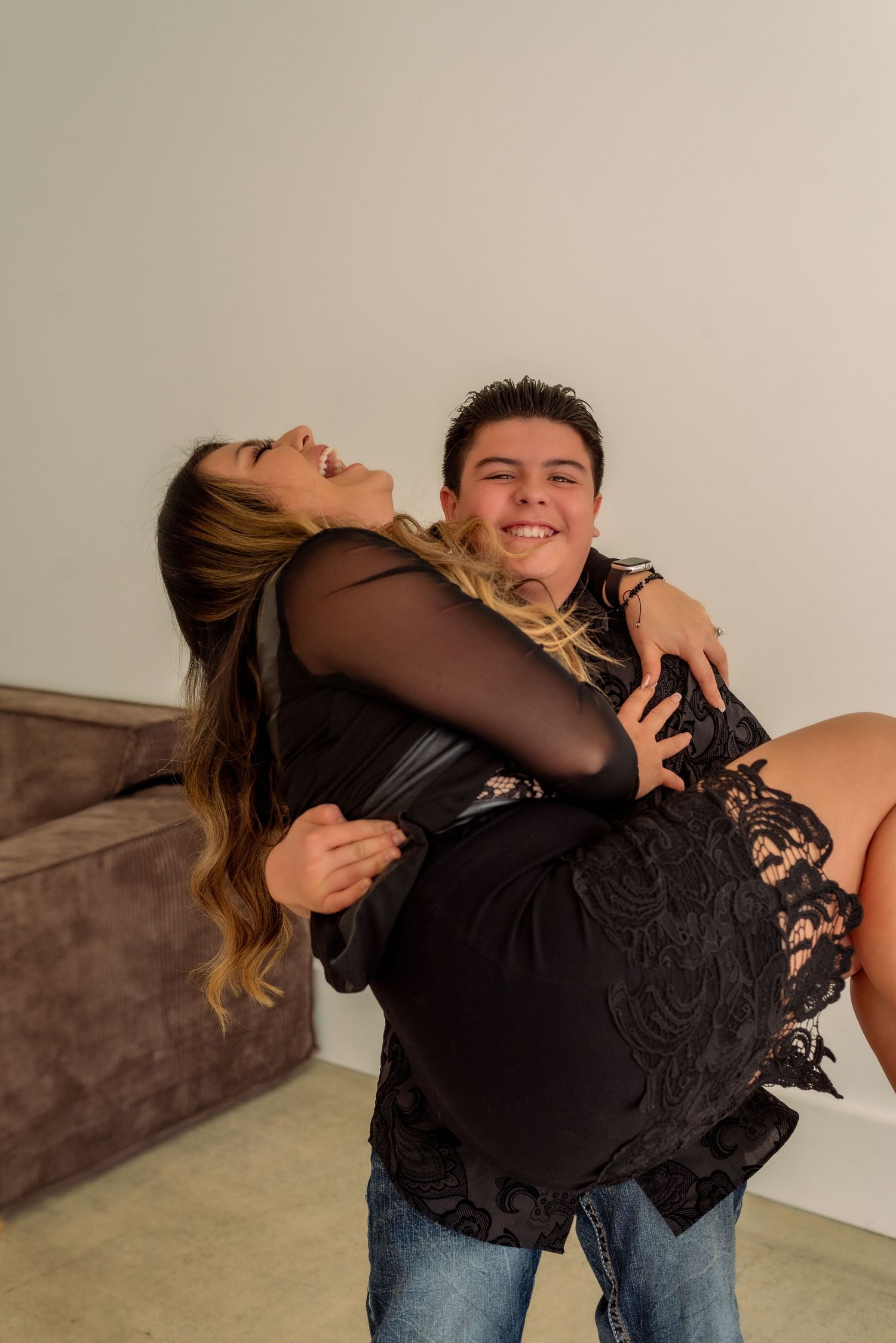 Couple in black attire sharing playful moments during a studio photoshoot.