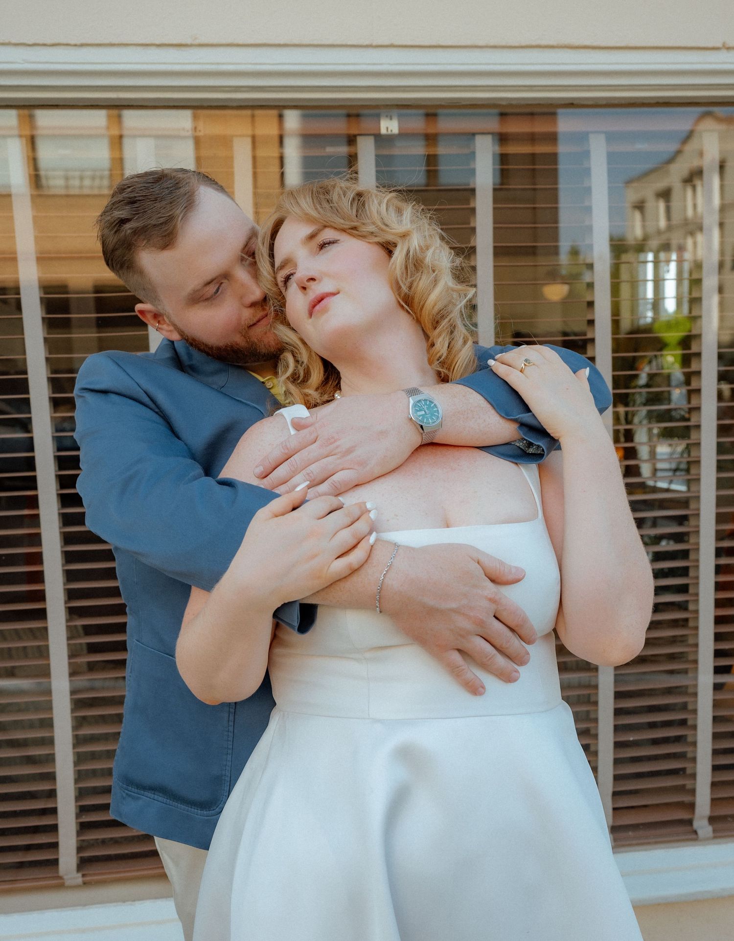 Tender embrace captured outside building with window blinds visible.