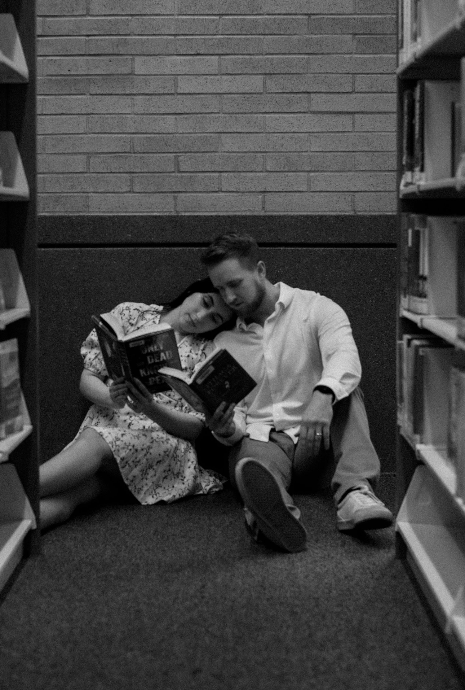 Black and white photos of a couple lying together between library shelves.