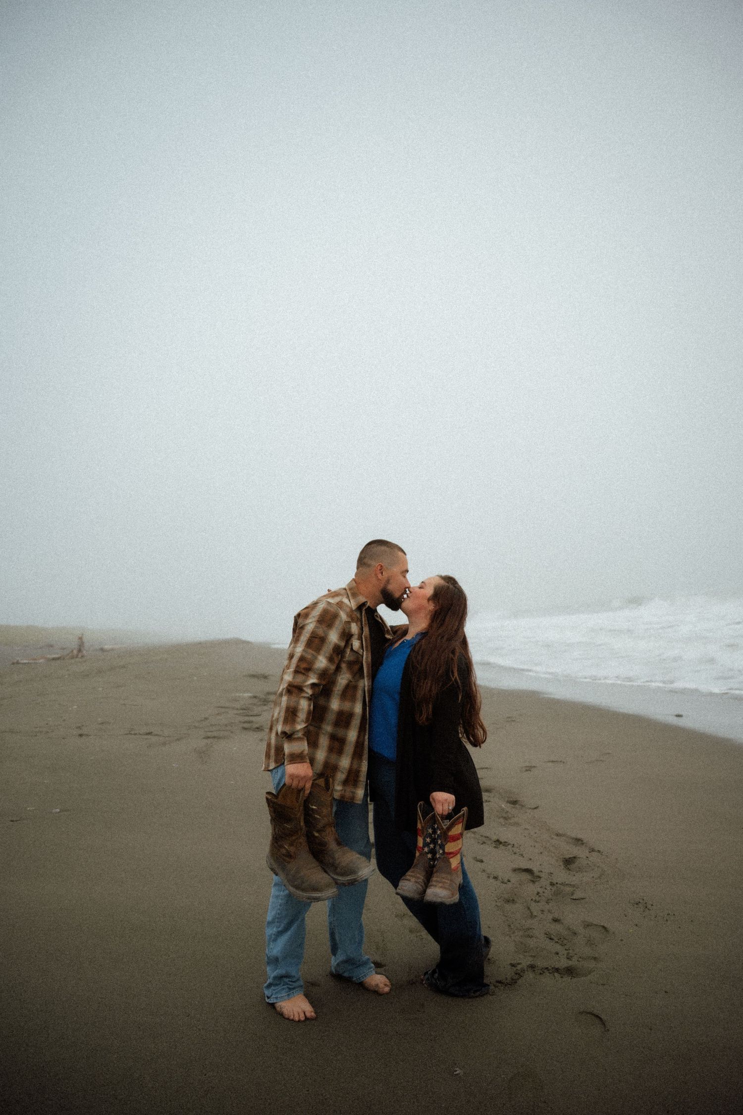 Two people share a playful moment on a moody beach shoreline.