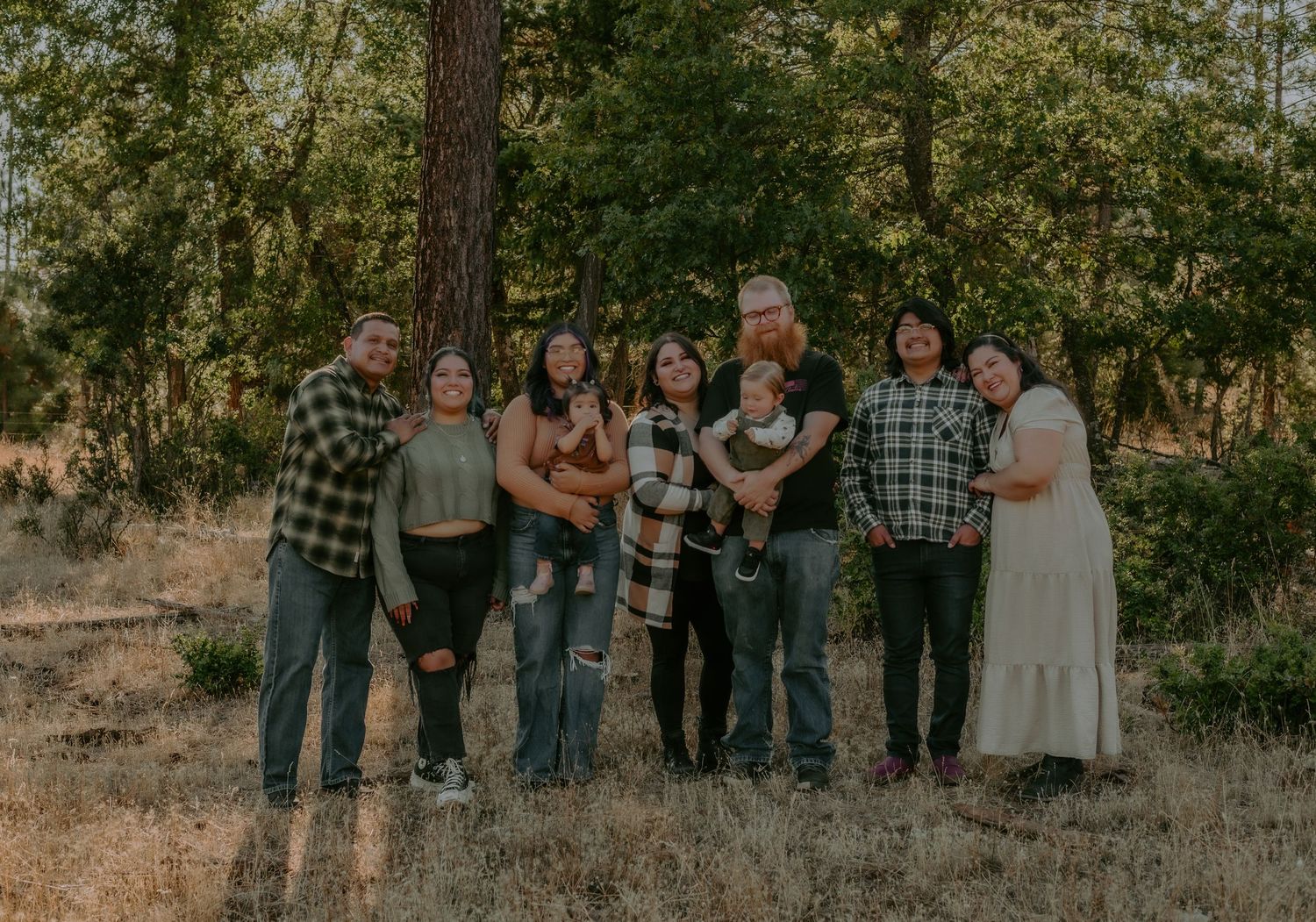 A group photo session in a wooded outdoor setting with pine trees and natural lighting.