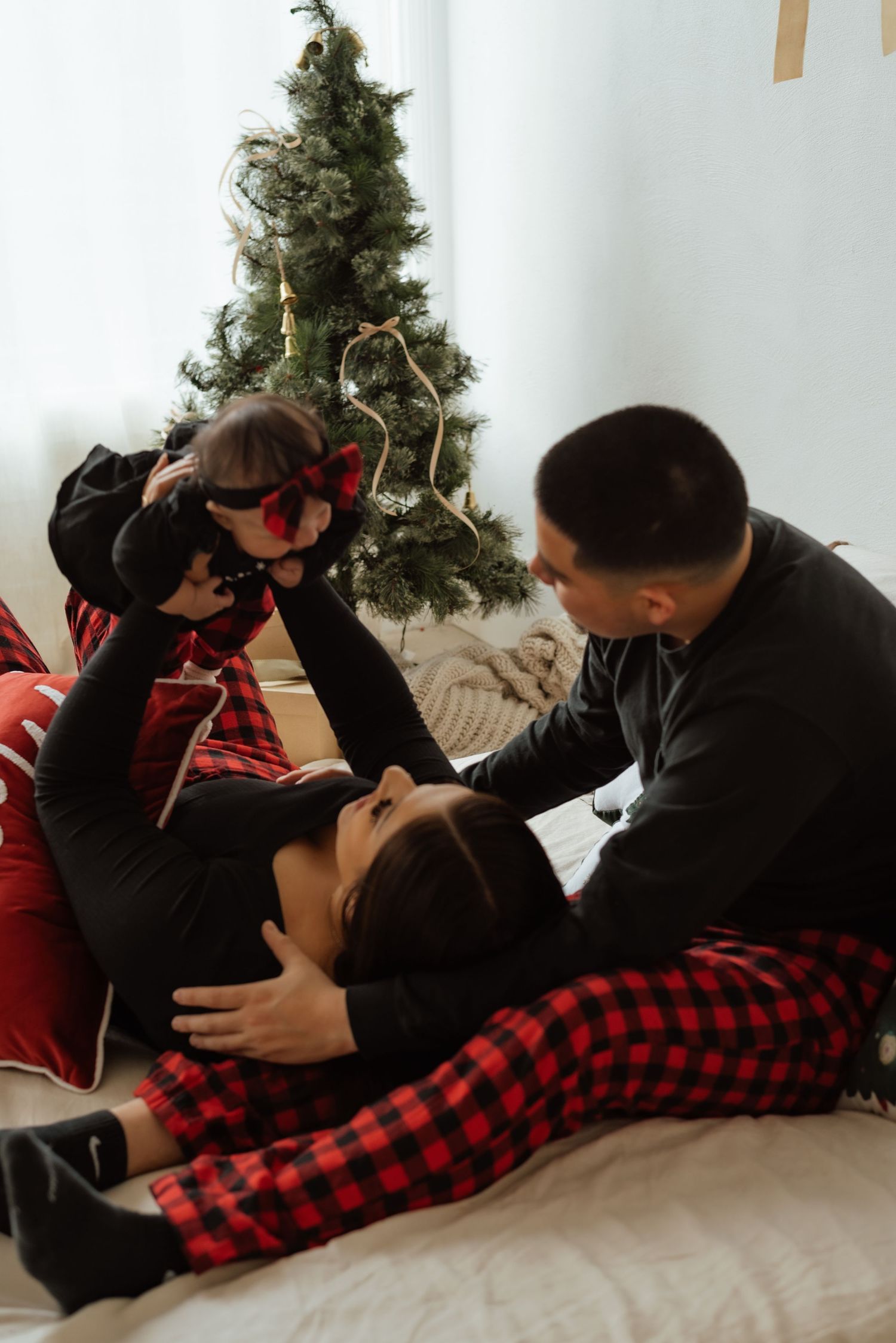 Couple in red plaid and black loungewear cuddling on white couch with Christmas decor.