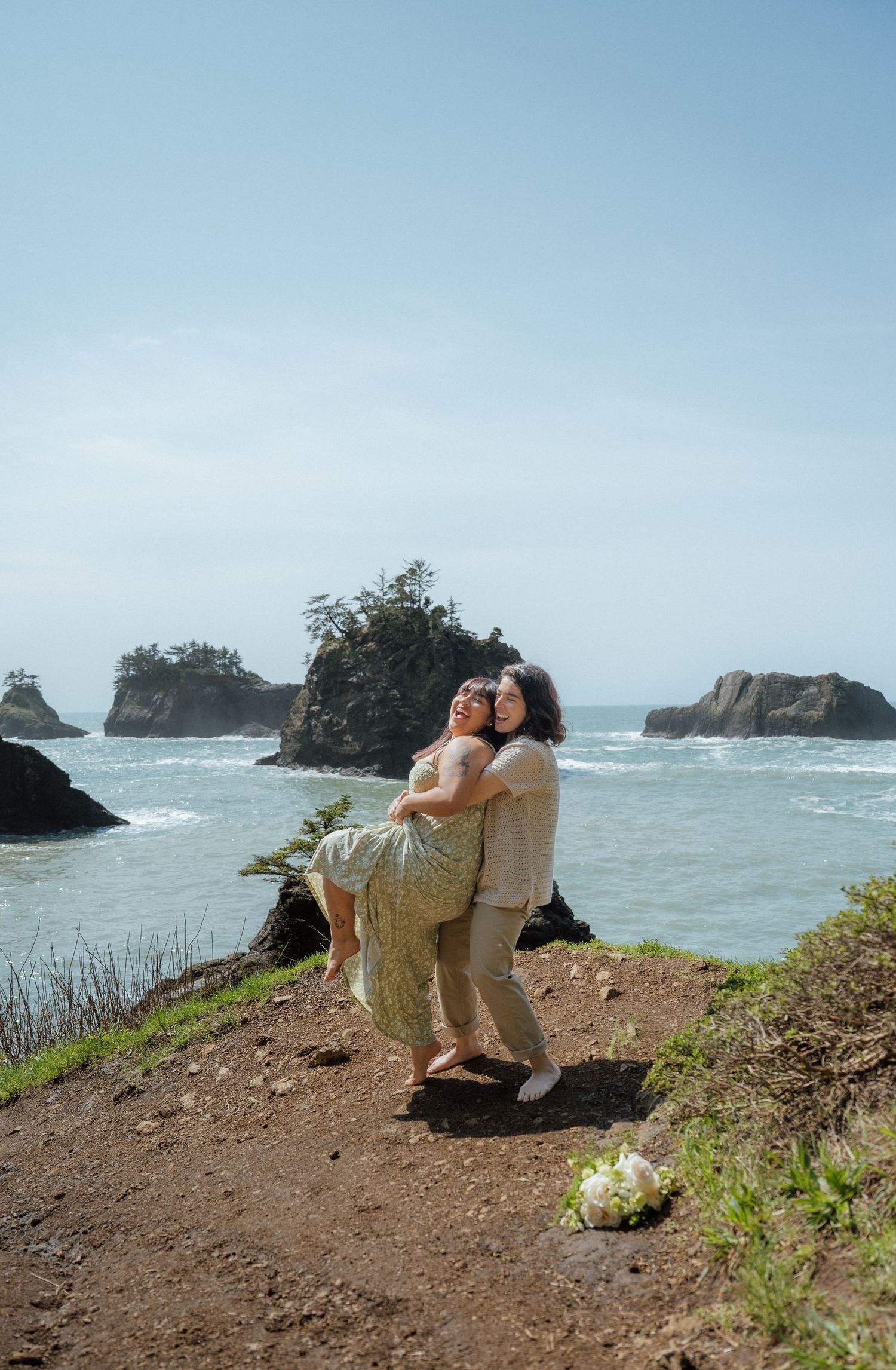 Couple shares an intimate moment on rugged coastal cliffs with crashing waves in the background.