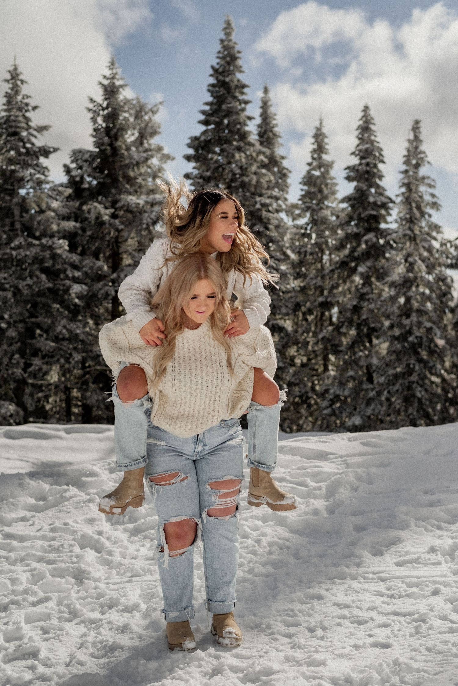 Playful piggyback ride in the snow wearing matching cream sweaters and distressed jeans.