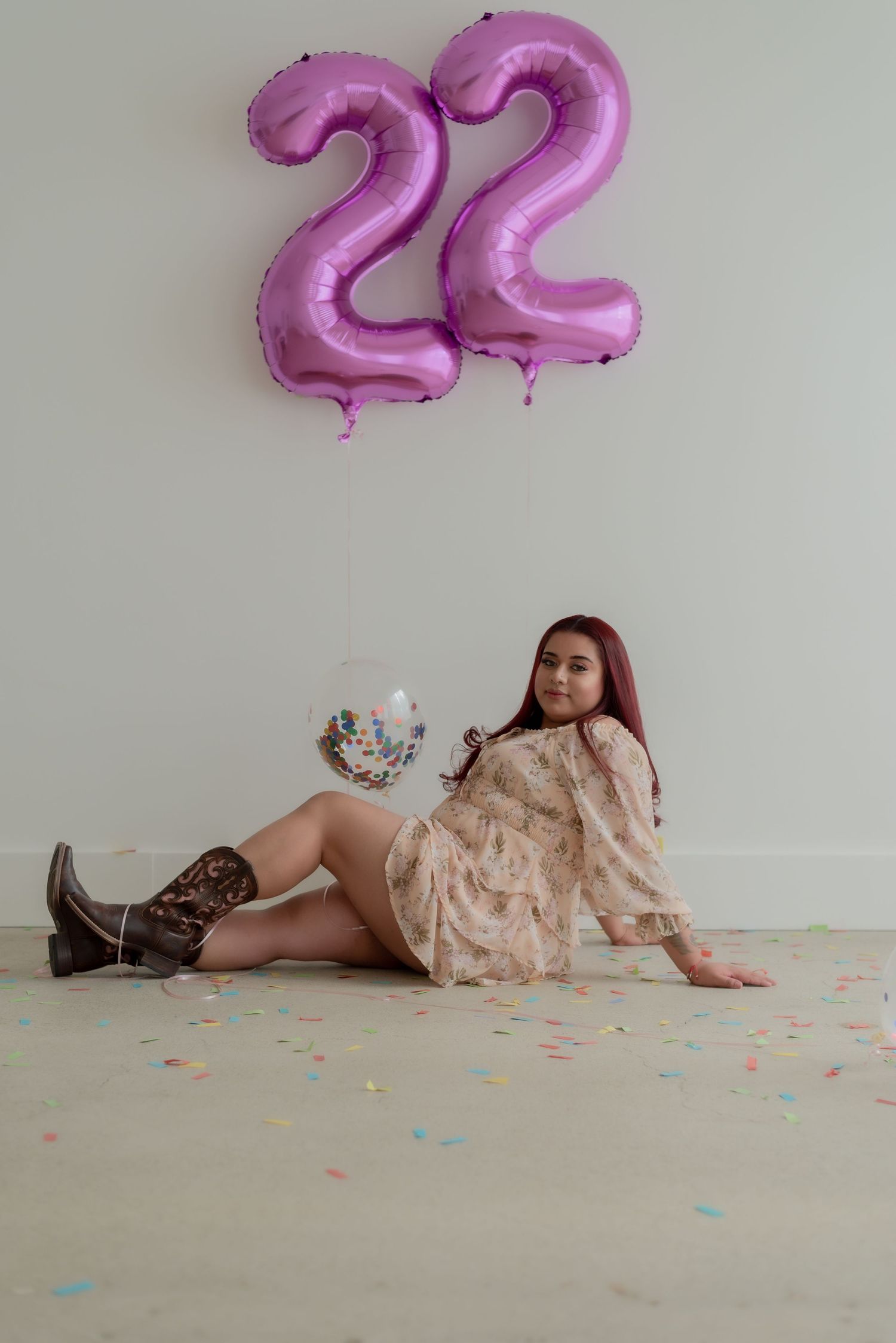 Celebratory scene with pink number 22 balloons, confetti, and someone posing in a peachy lace dress.