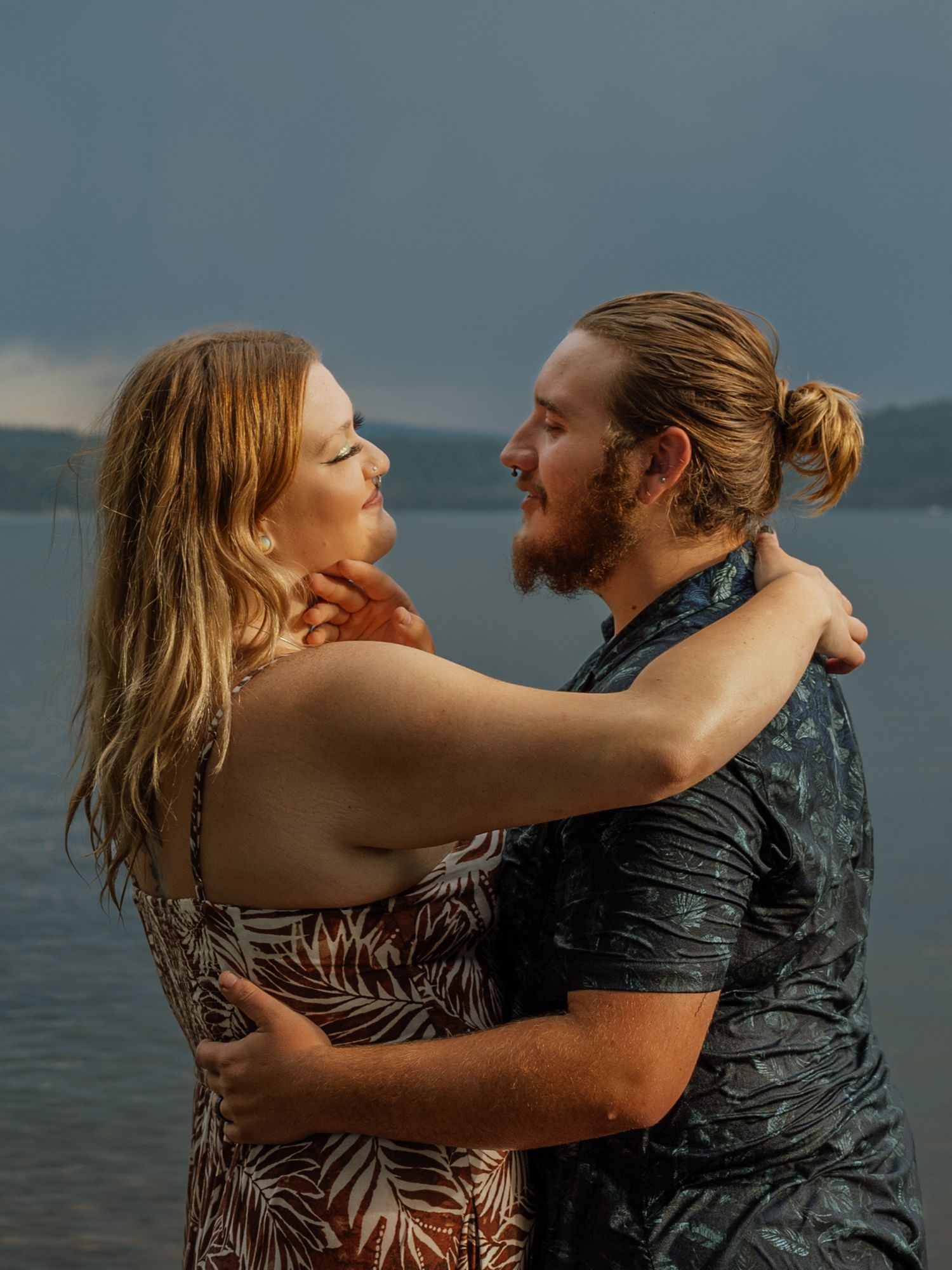 A couple shares a joyful embrace while standing in water with mountains in the background.