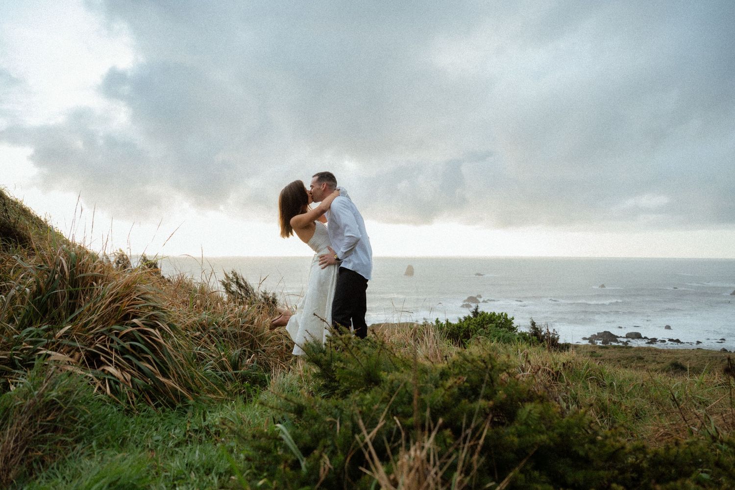 Dramatic coastal landscape photography with figures silhouetted against cloudy skies.