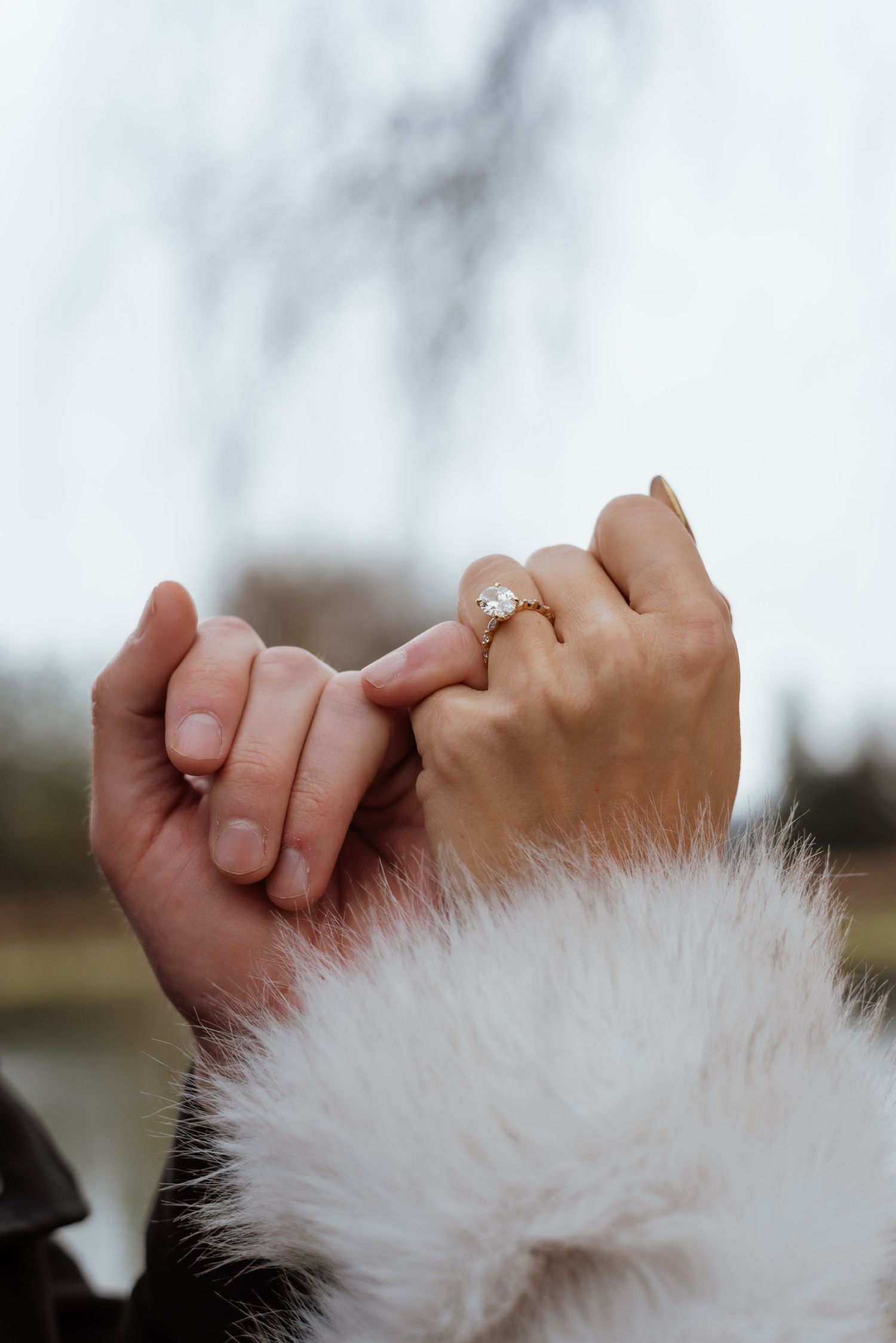 Close-up of intertwined hands with engagement ring against winter backdrop.