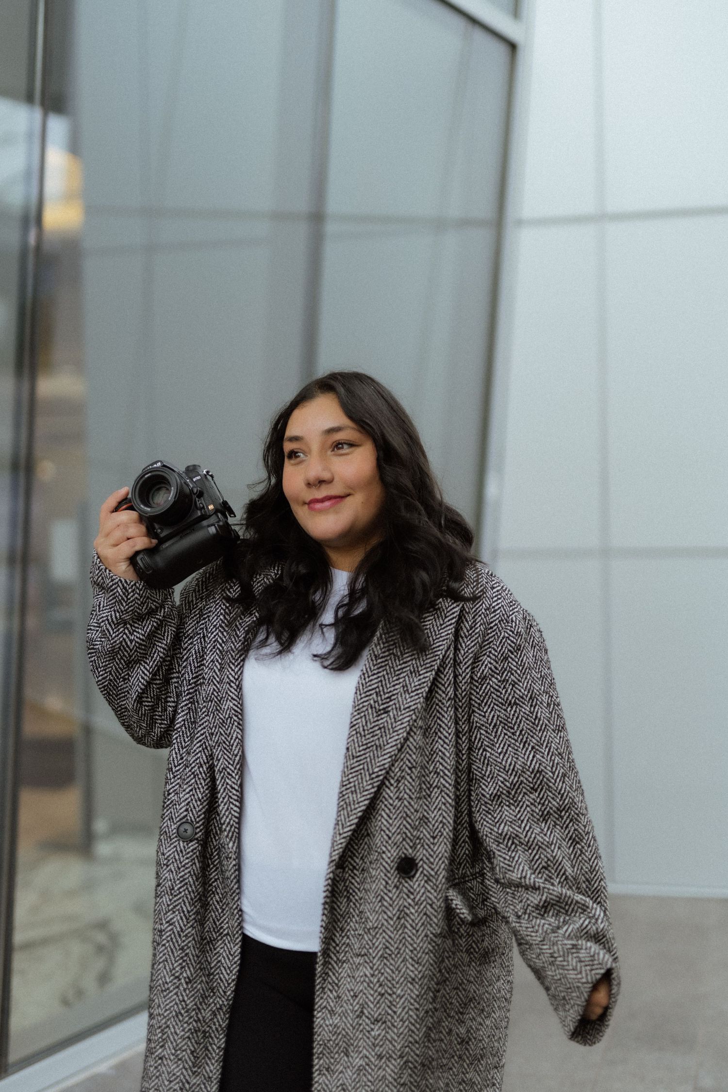 Woman in gray coat and white top poses playfully in three different shots against modern building exterior.