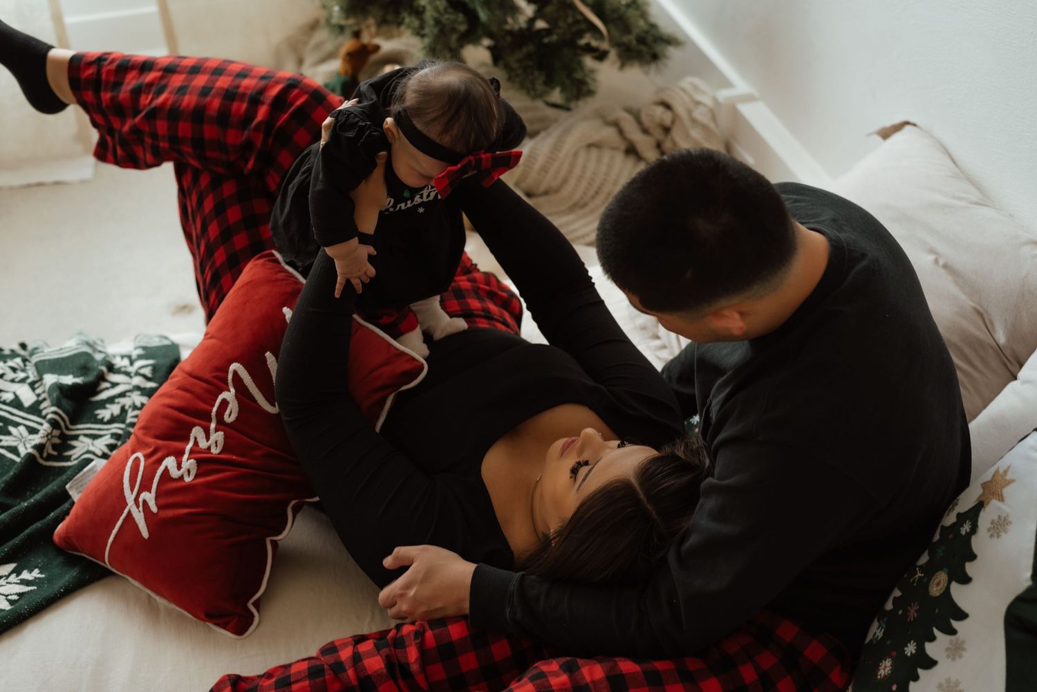 Intimate holiday photos of couple in matching pajamas on white couch with Christmas tree.