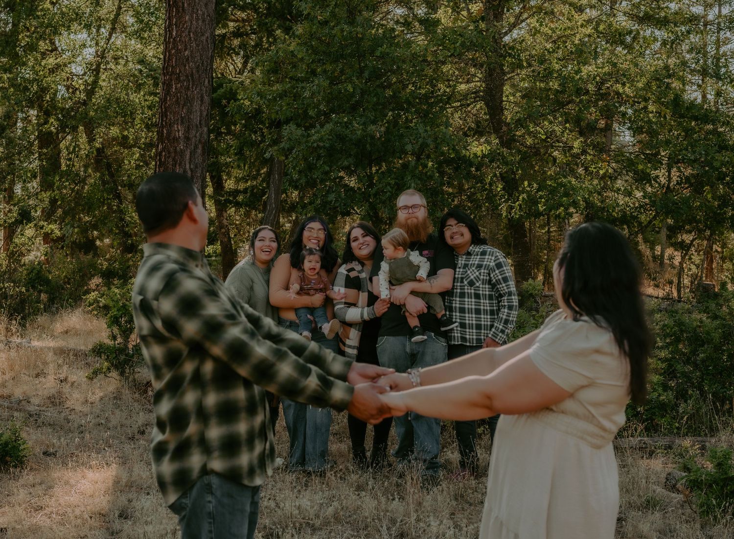 Family gathering posed together against a backdrop of tall pine trees at sunset.