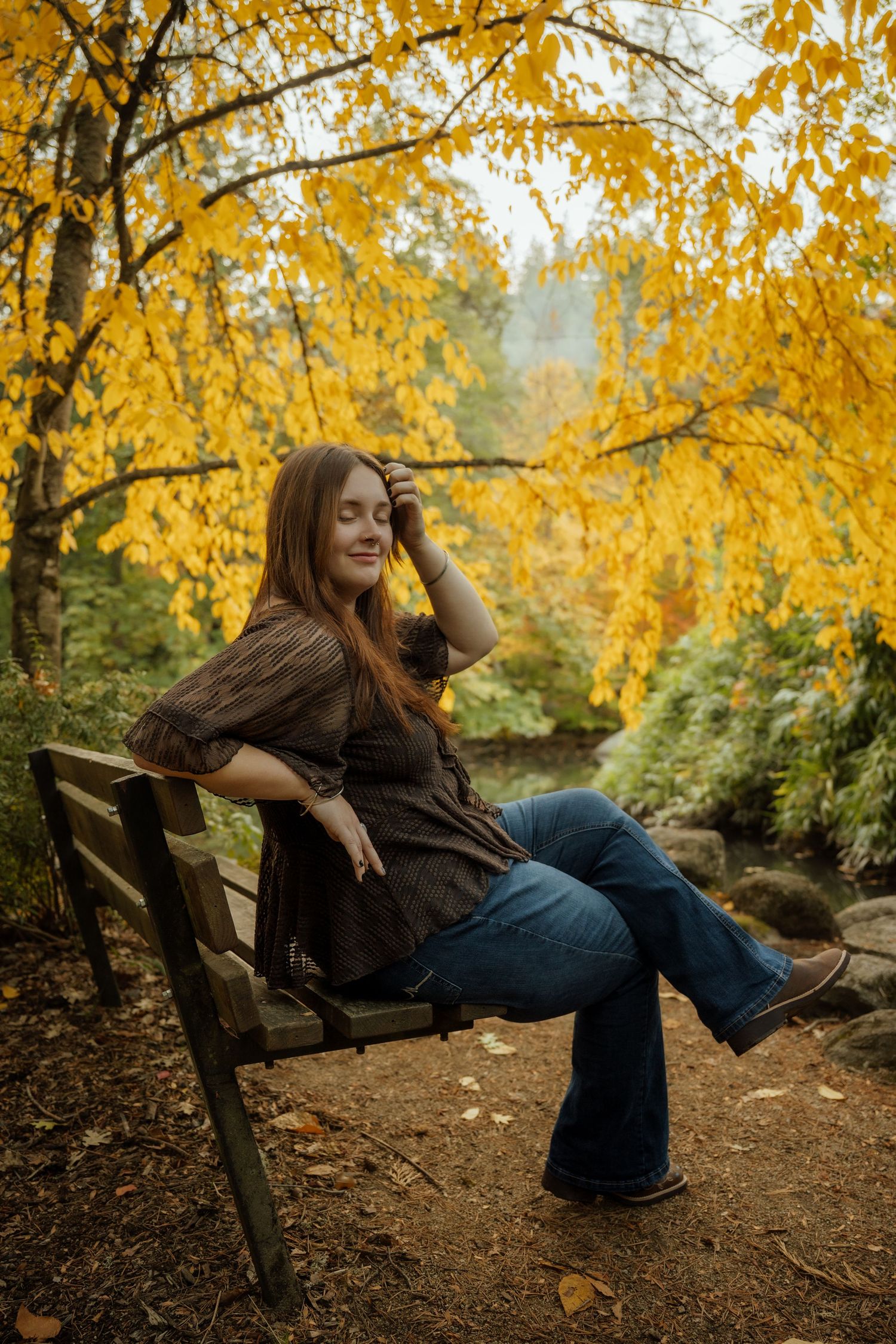 Person relaxes on wooden bench surrounded by vibrant yellow autumn foliage in forest setting.