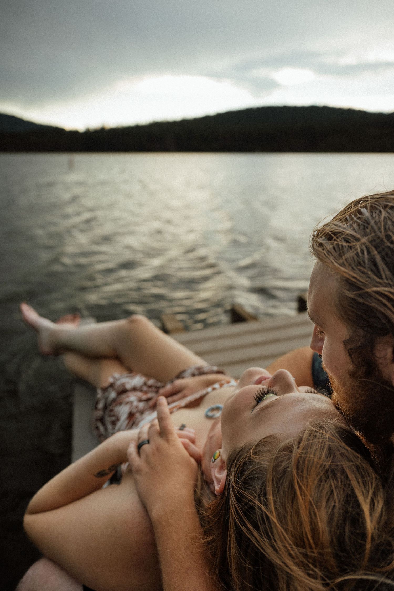 Two people lying close together on a dock by a scenic mountain lake.