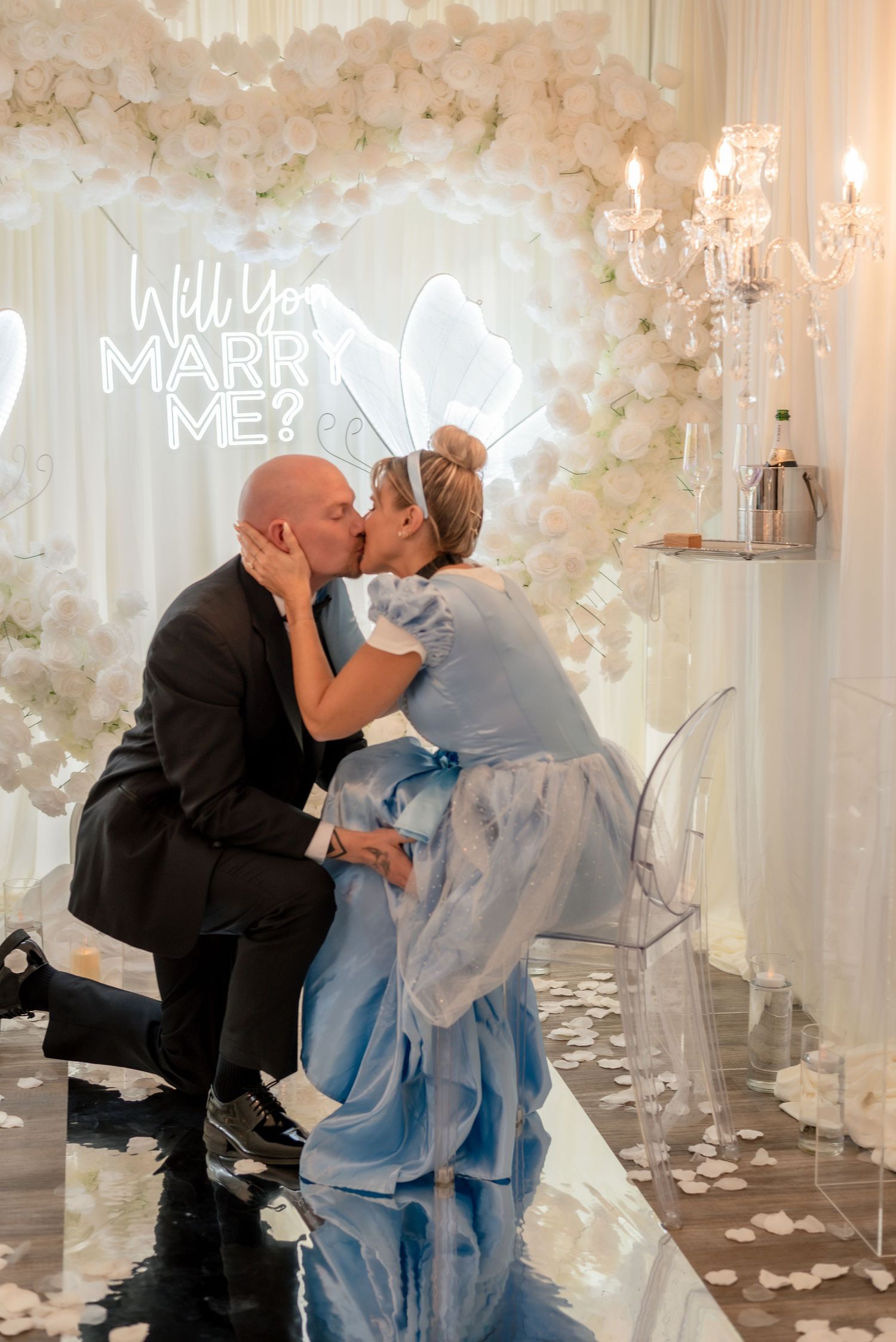 Couple kisses after proposal in beautifully decorated room with white floral backdrop and neon signage.