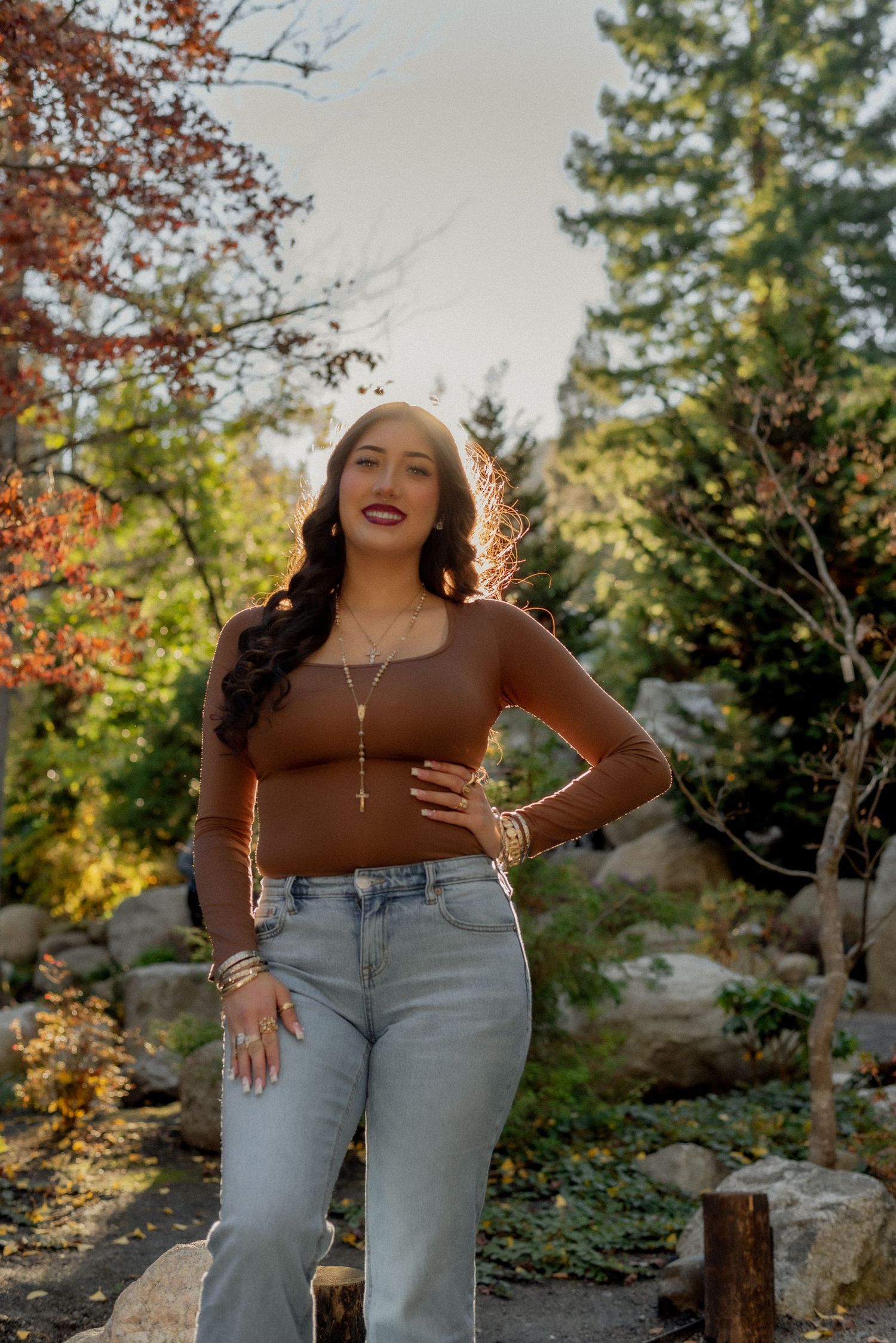 Casual autumn fashion photoshoot in a park setting with light brown top and jeans against fall foliage.