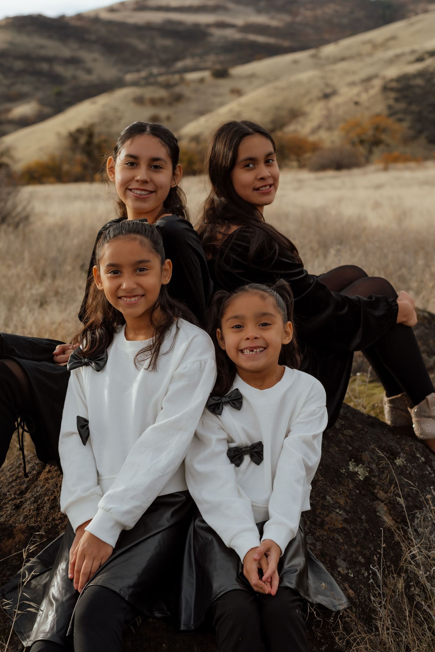 Children in white outfits sit together on rocks with mountain landscape behind.