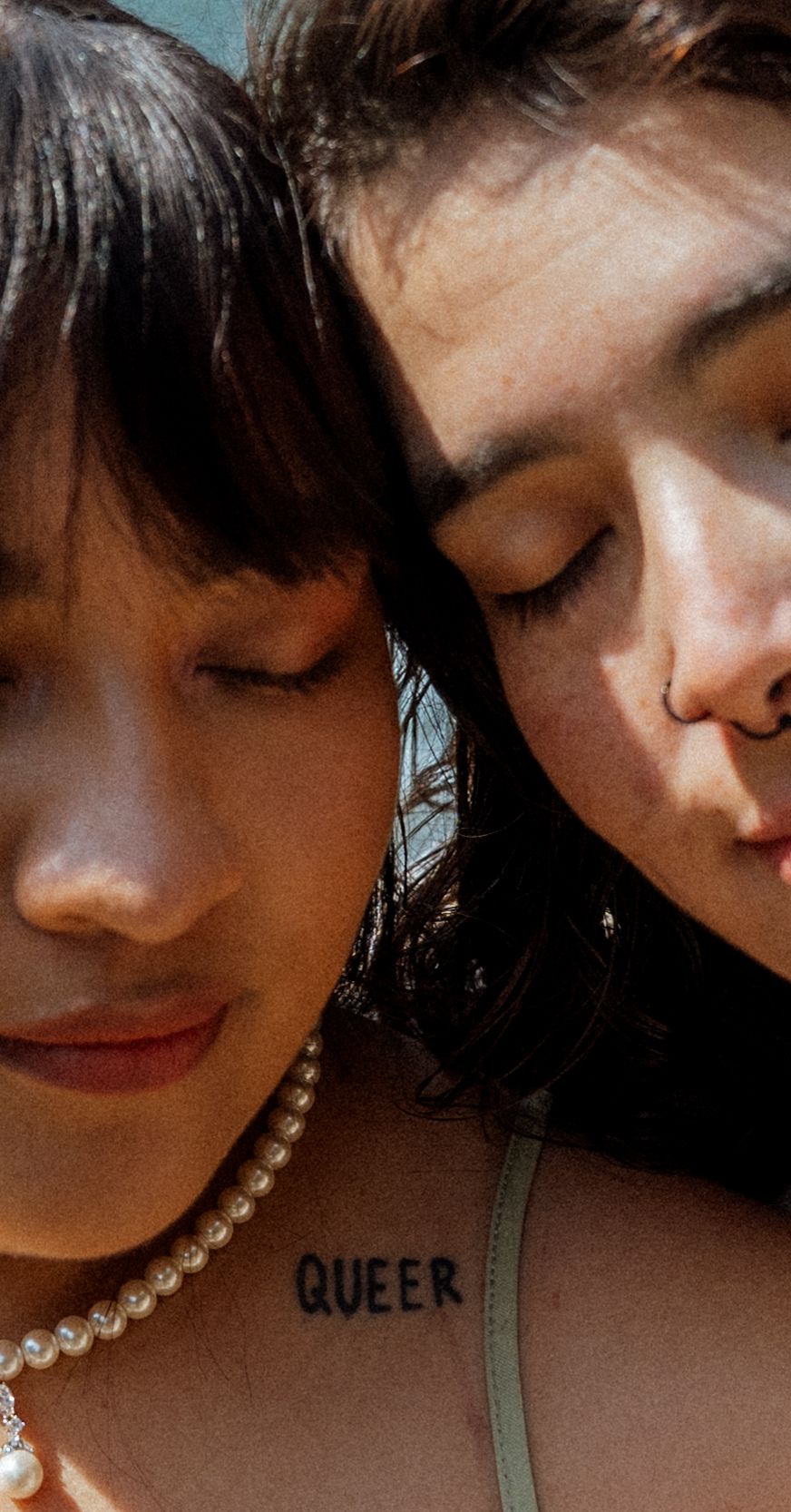 Close-up portrait of two people with pearl necklace and closed eyes in intimate pose.