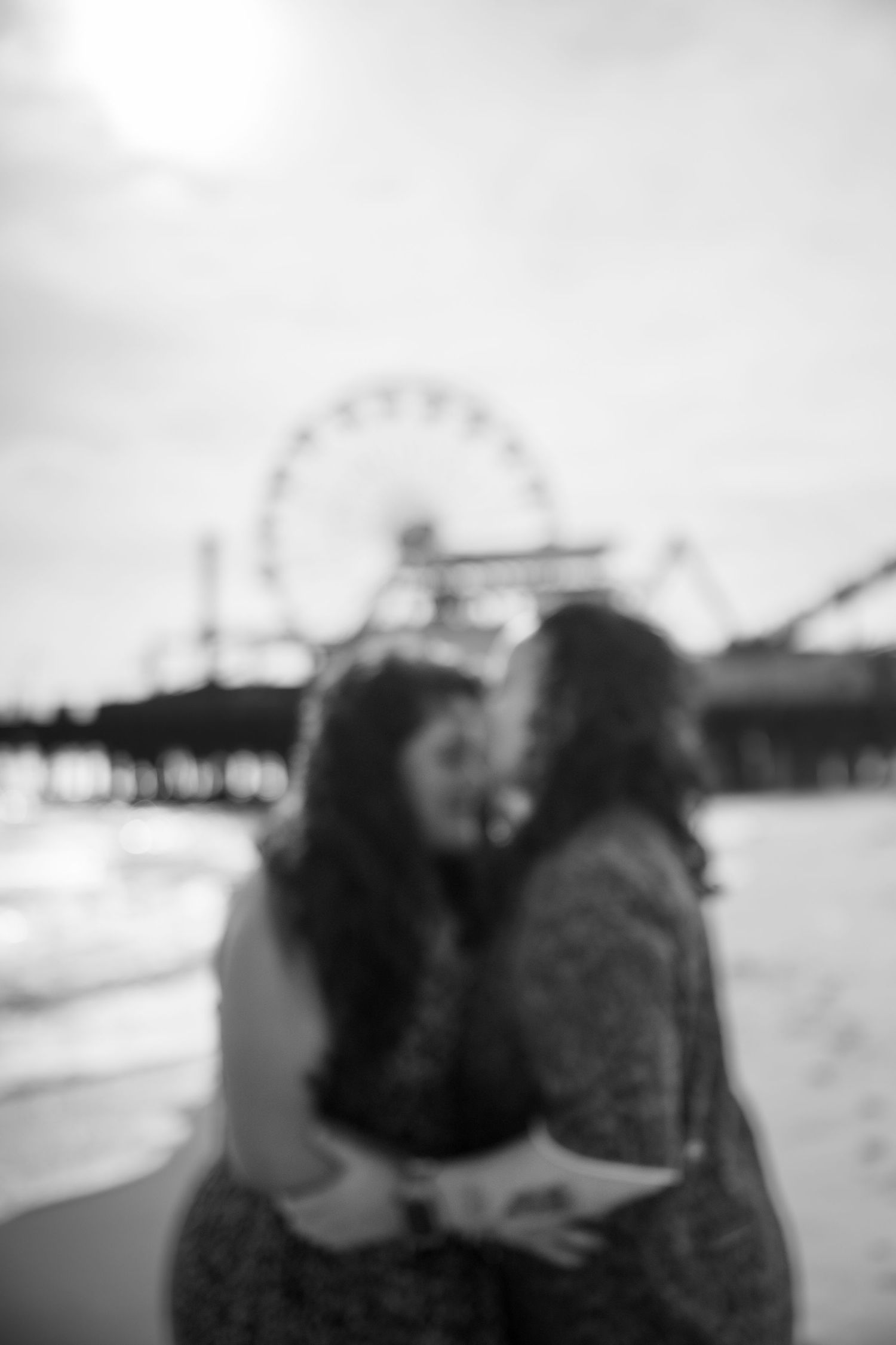 A blurred black and white photo of a couple at a pier with a ferris wheel in the background.