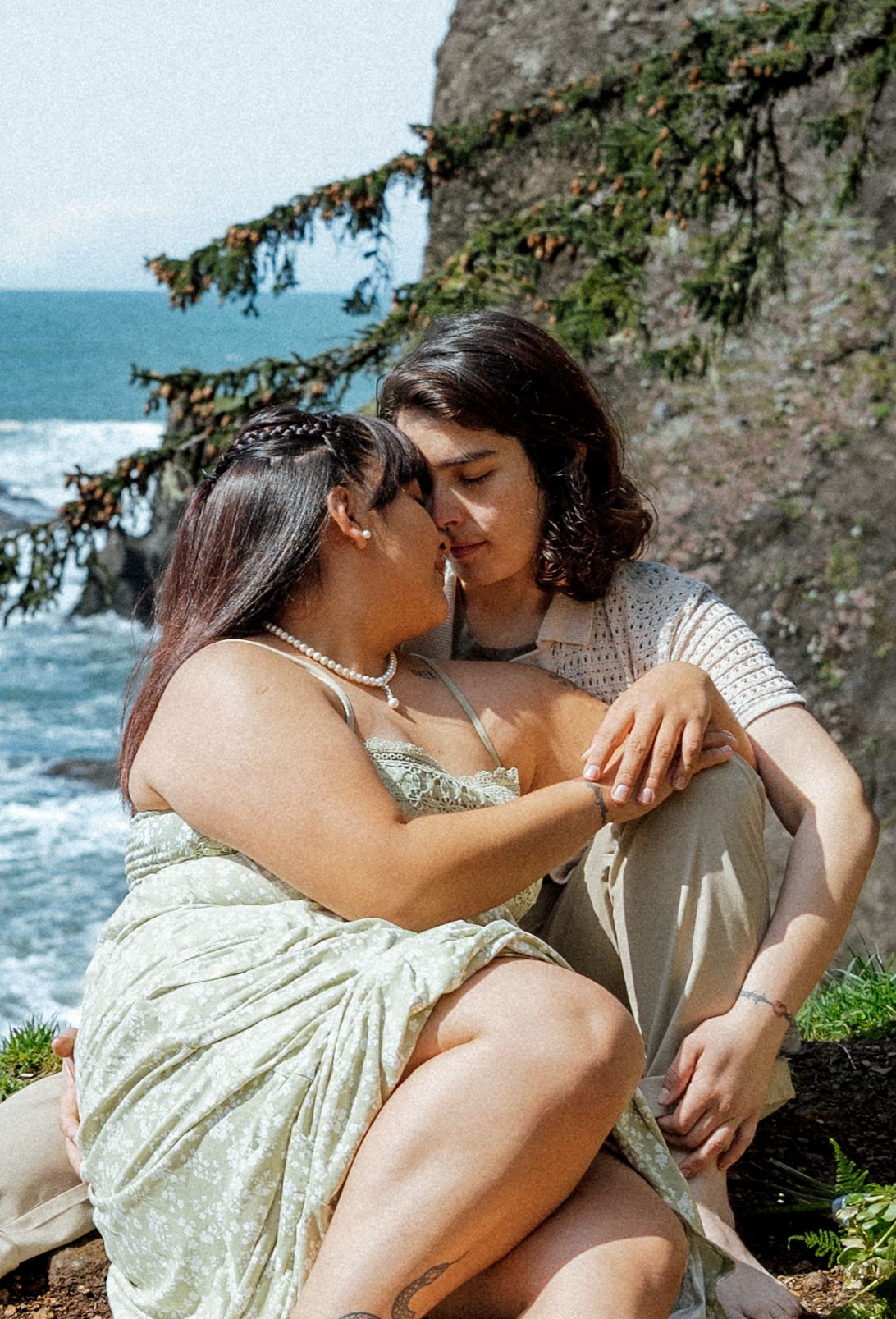 A romantic moment shared between two people on a coastal cliff overlooking the ocean.
