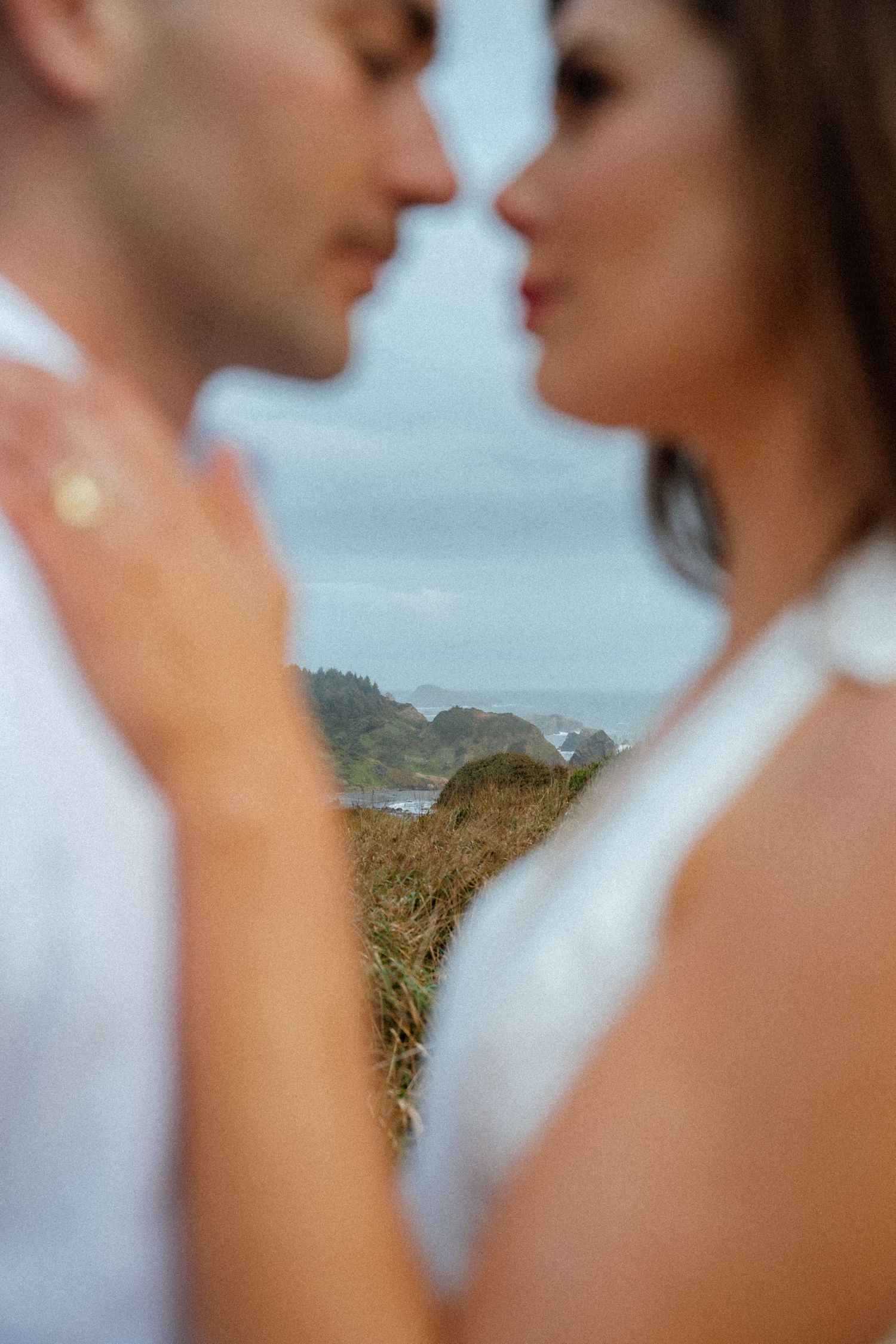 An artistic close-up shot of a couple about to kiss with coastal scenery in background.