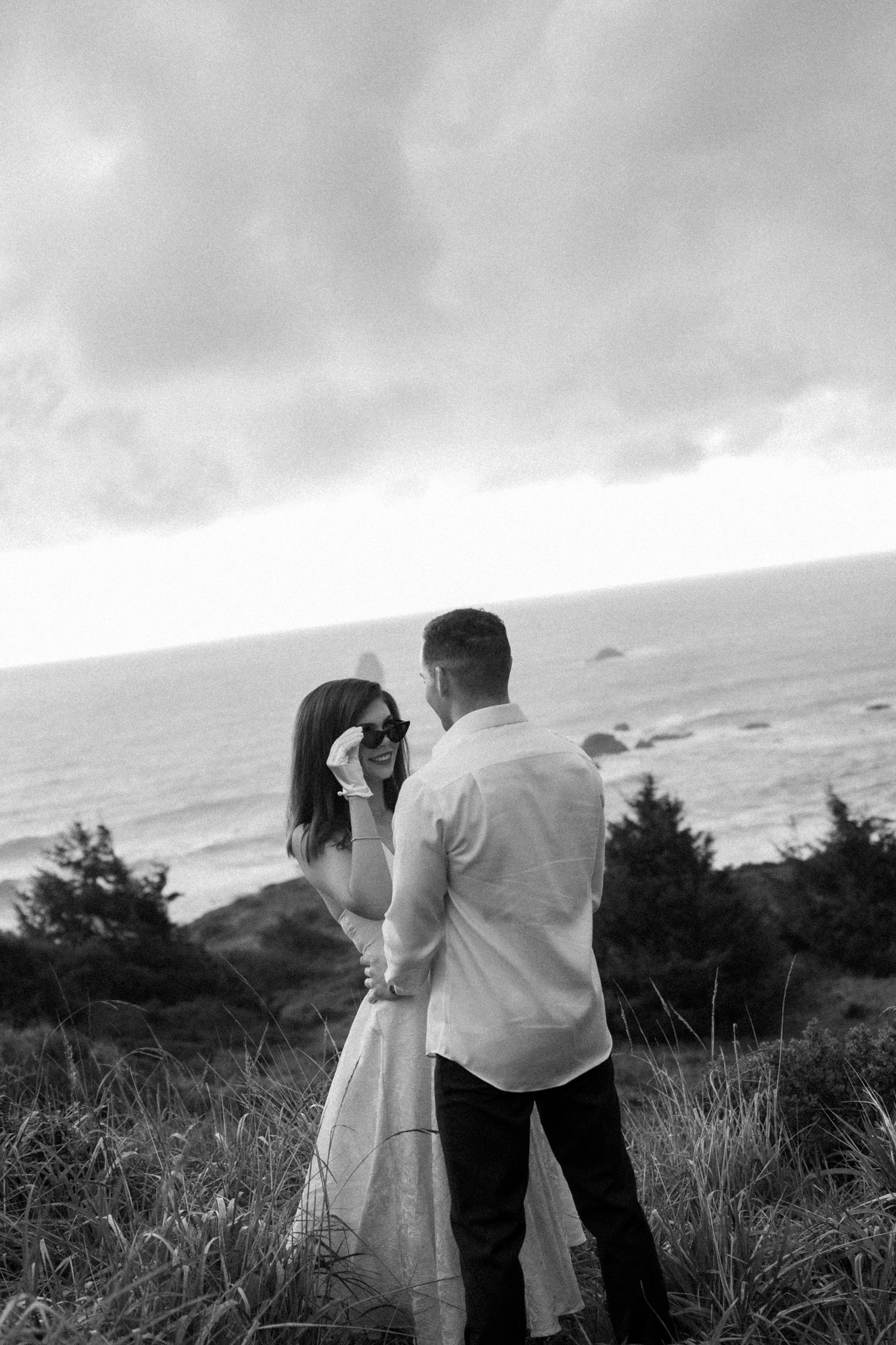 A romantic black and white portrait of a couple on a coastal cliff.