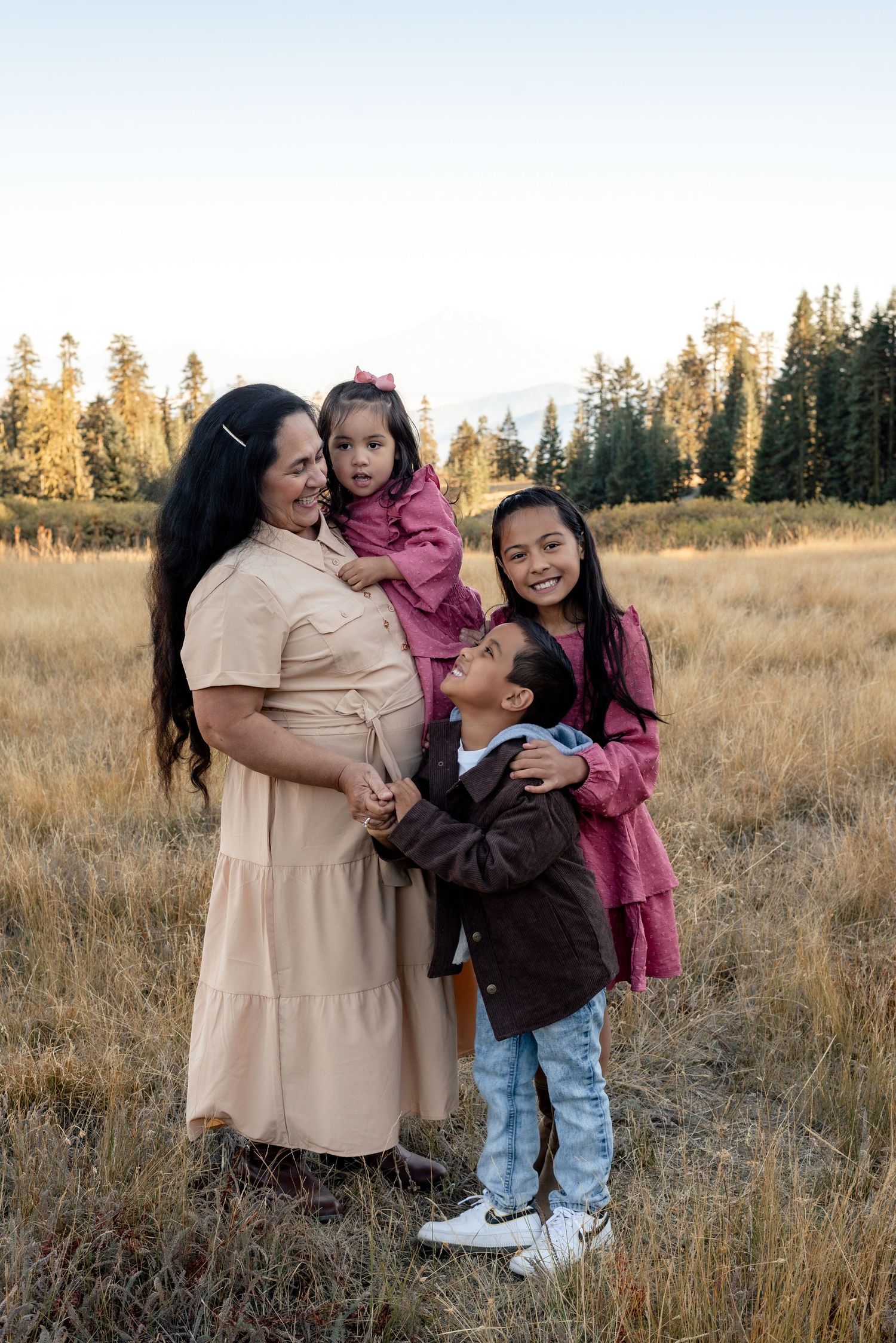 Family sharing joyful moments together in a golden field with pine trees.
