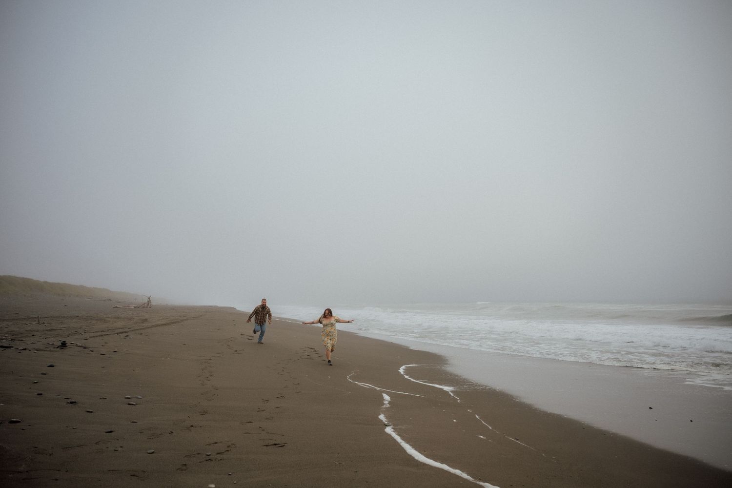 A distant view of people walking along a misty beach shoreline.