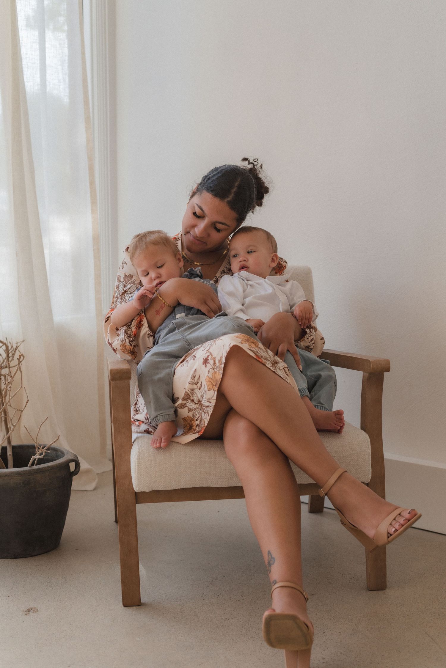 Relaxed scene of caregiver and babies lounging together on wooden chair in sunlit room.