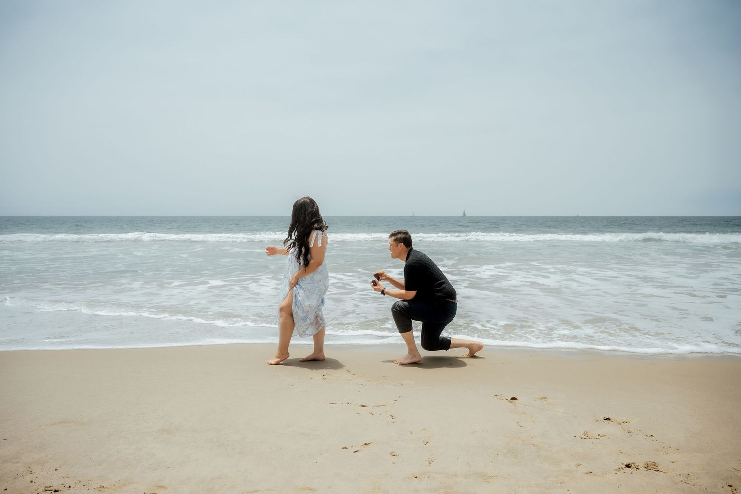 A proposal scene unfolding on a misty beach with waves crashing in the background.