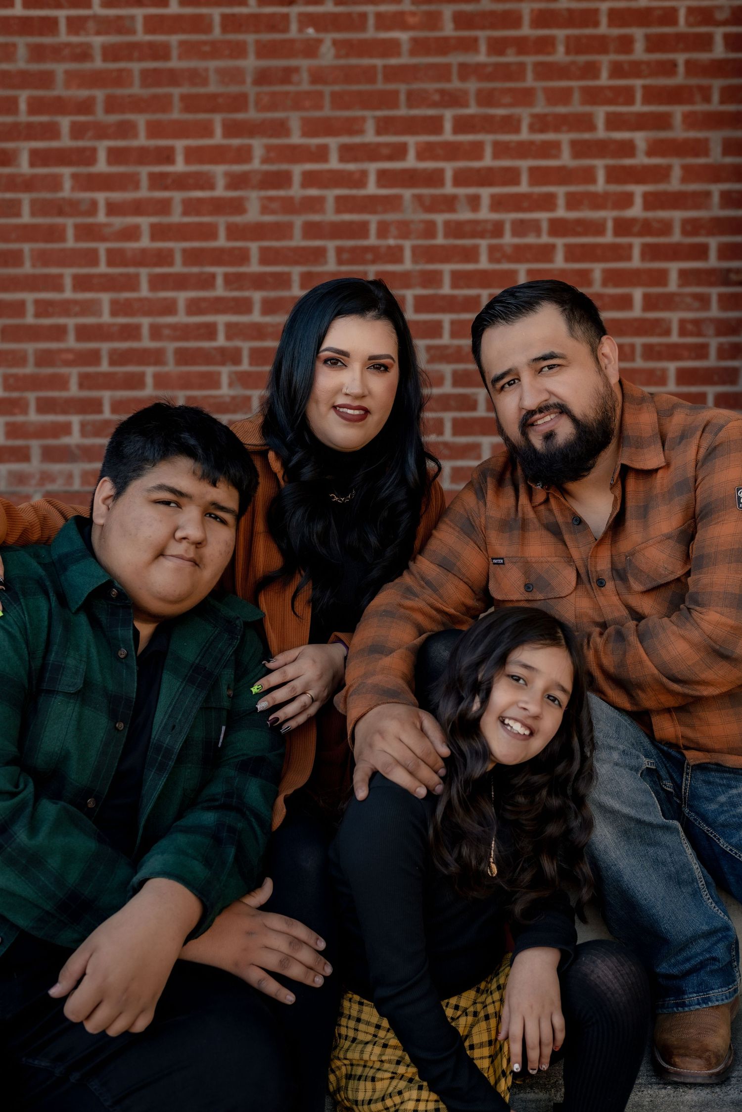 Family portrait against a red brick wall wearing coordinated fall colors.