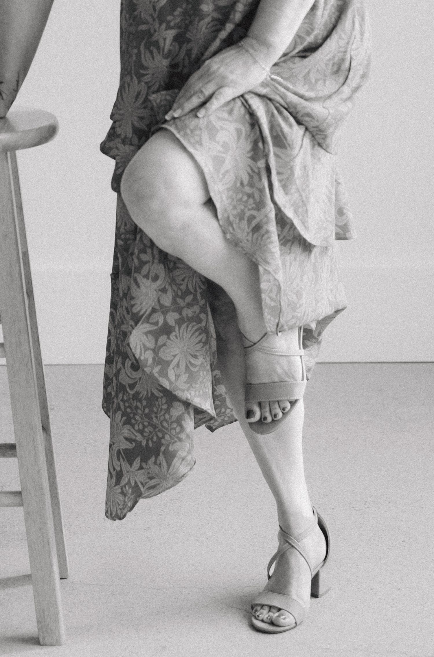 Close-up view of floral dress and sandals on feet against a white background.