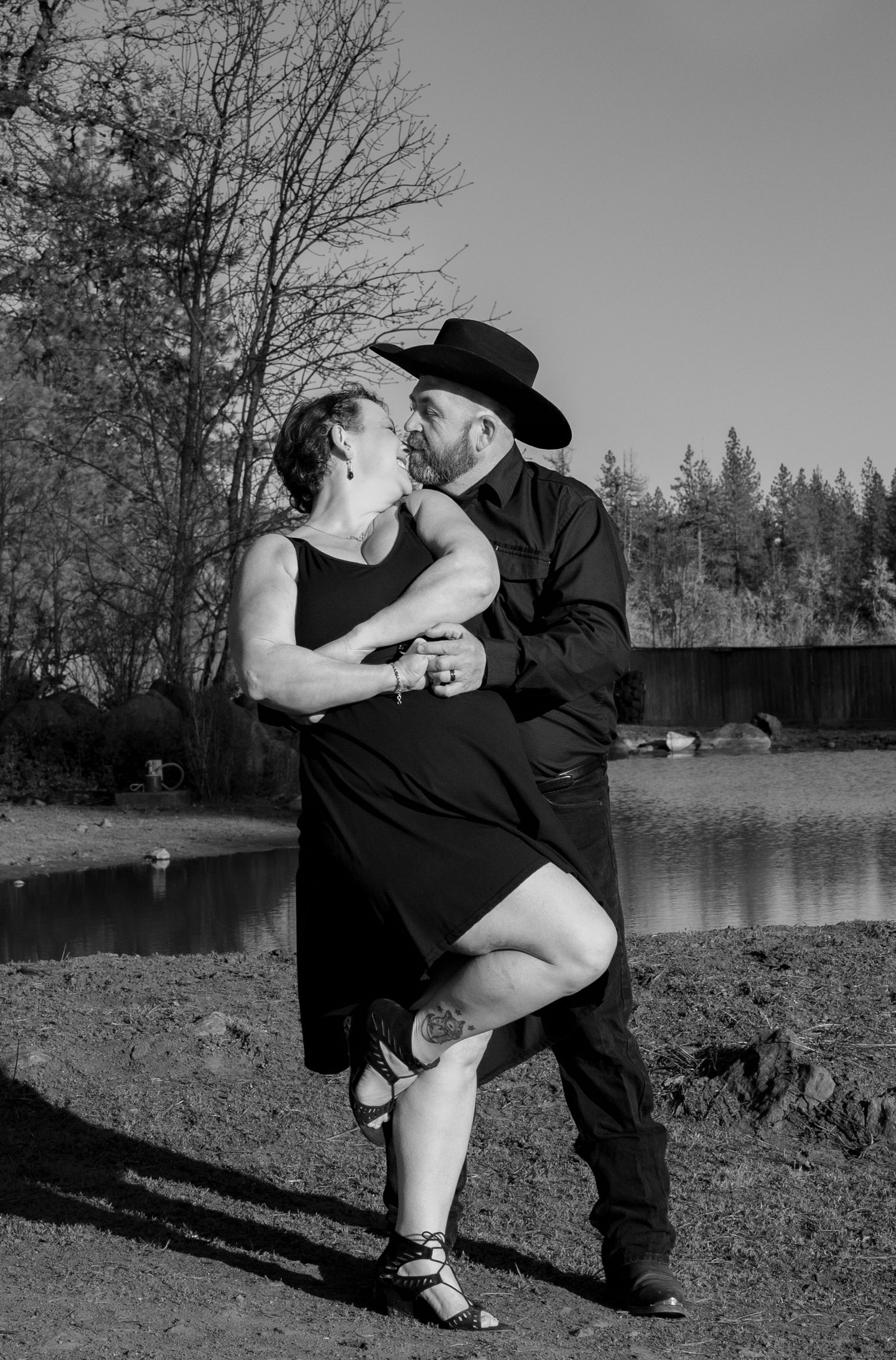 A black and white photo of a couple dancing outdoors near a lake.