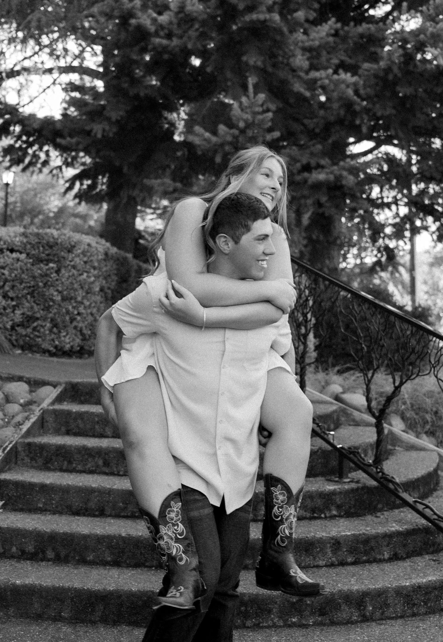 A black and white photo of a couple sitting together wearing cowboy boots.