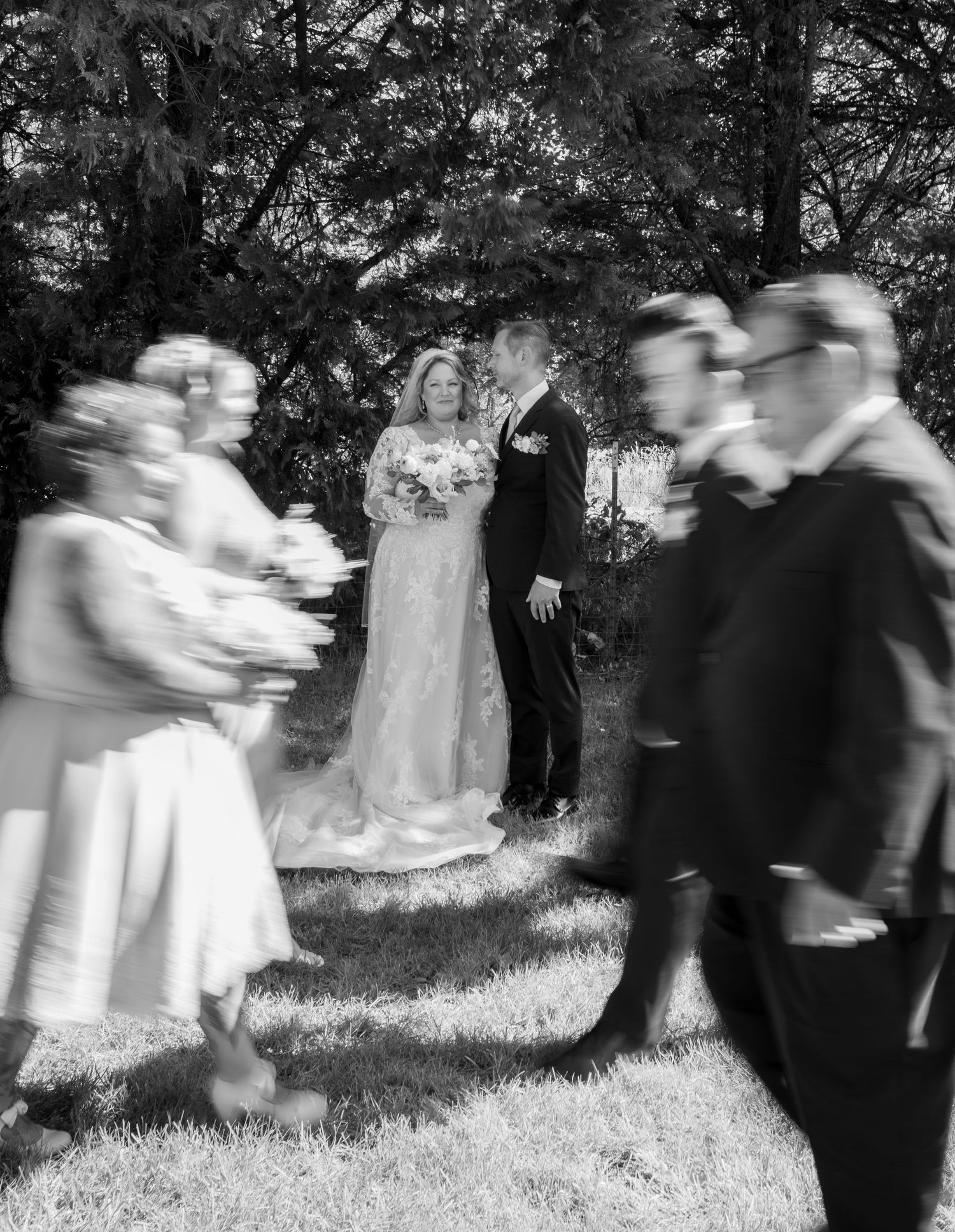 Motion blur captures wedding party walking through garden in black and white photography.