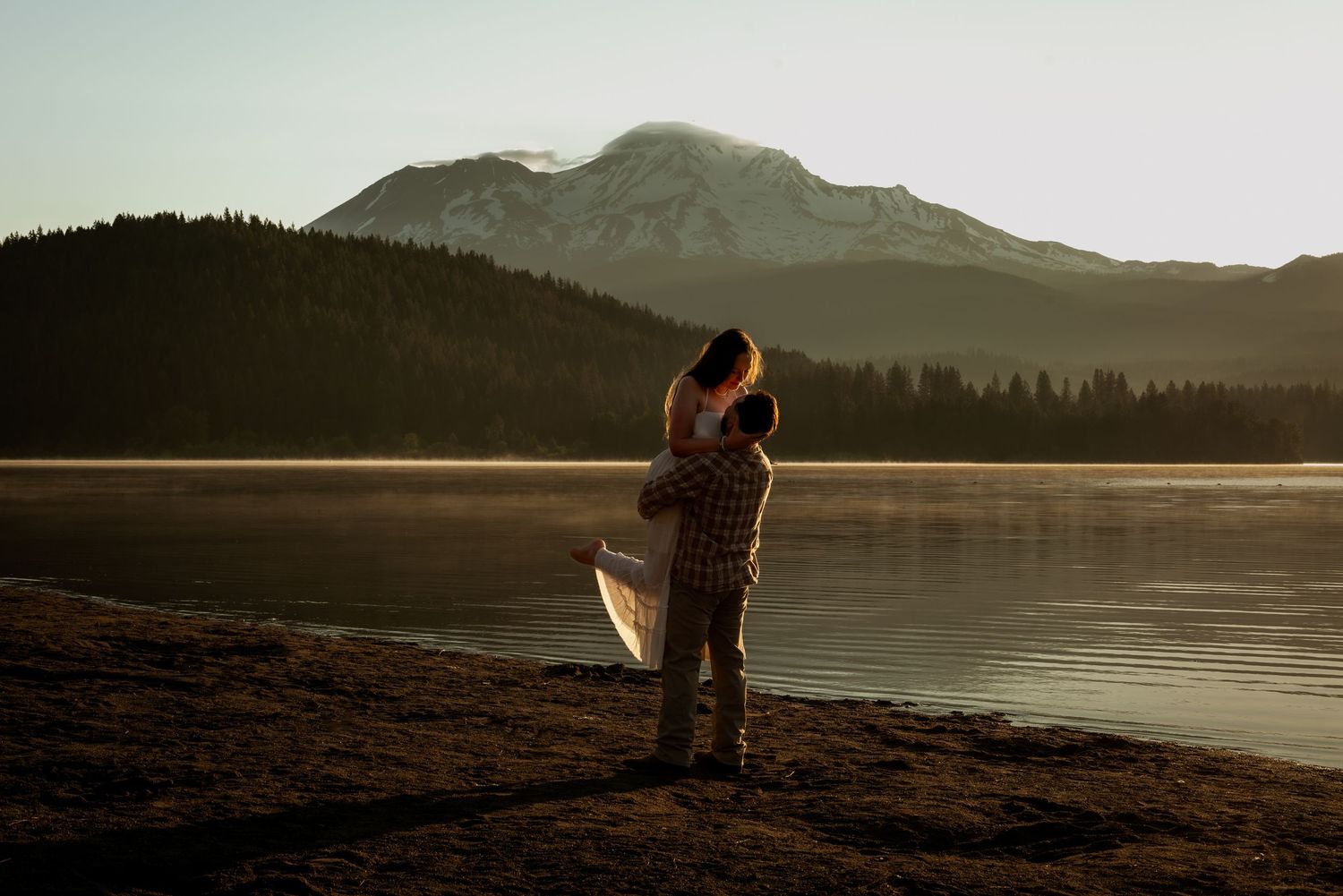 Silhouetted couple embraces against dramatic mountain lake sunset landscape.