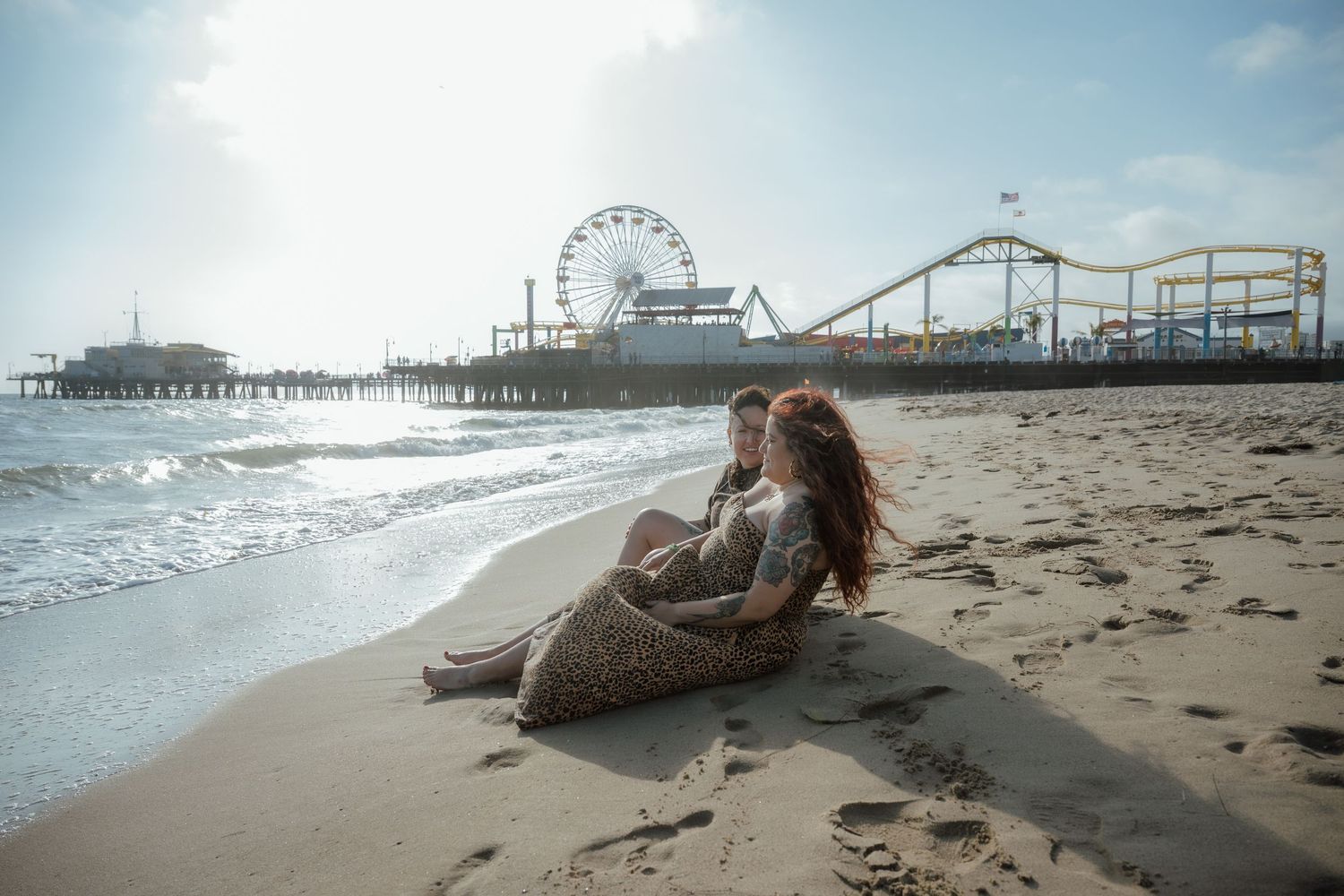 Scenic beach view with pier, Ferris wheel, and roller coaster visible in the distance on a sunny day.
