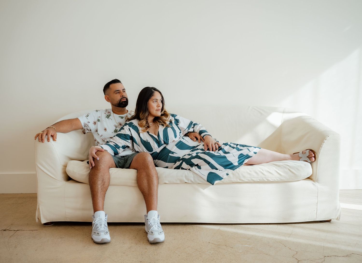 A couple lounges together on a white couch wearing matching blue and white patterned outfits.